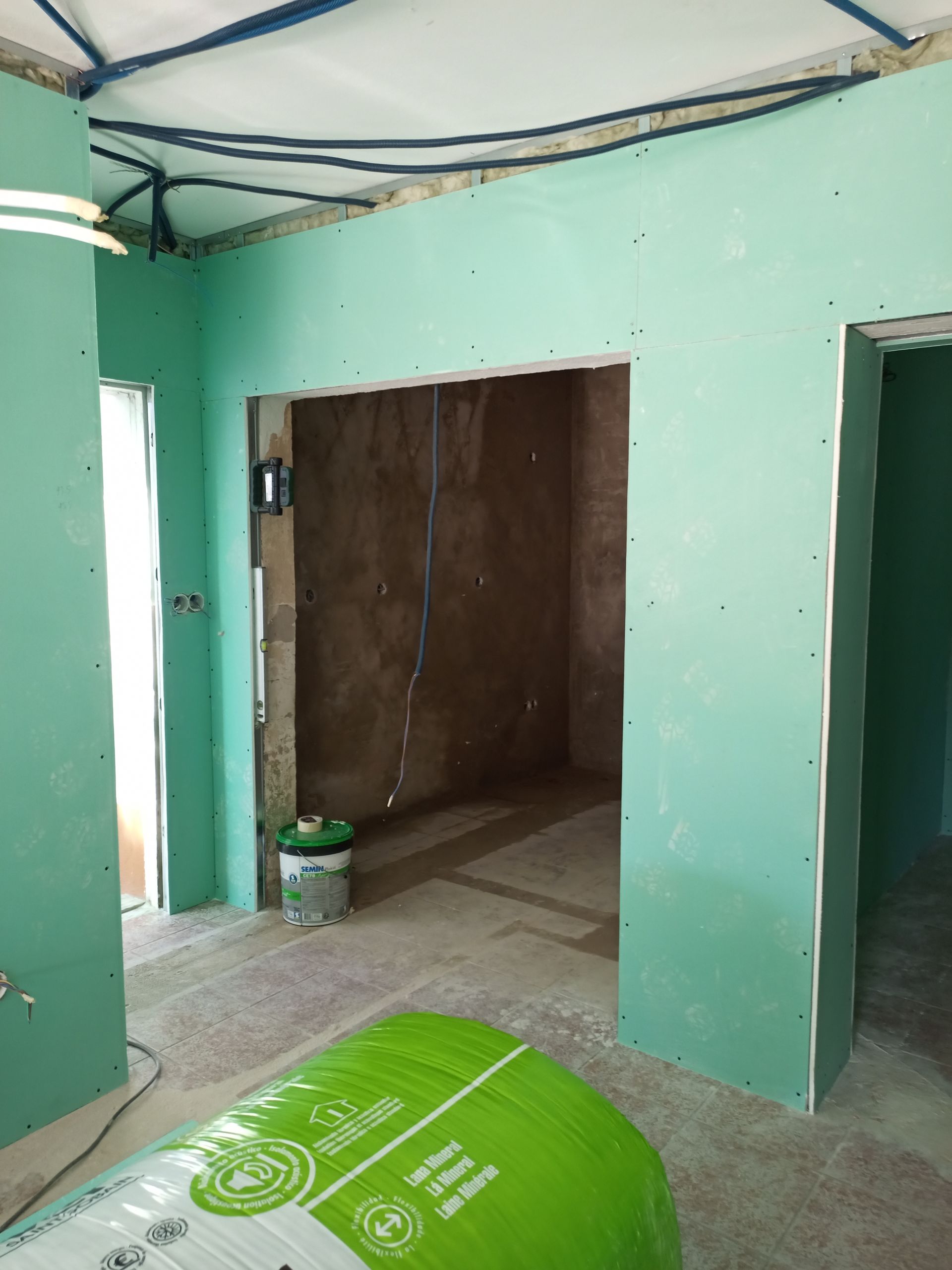 Sala em construção com paredes de gesso verde e portas abertas.