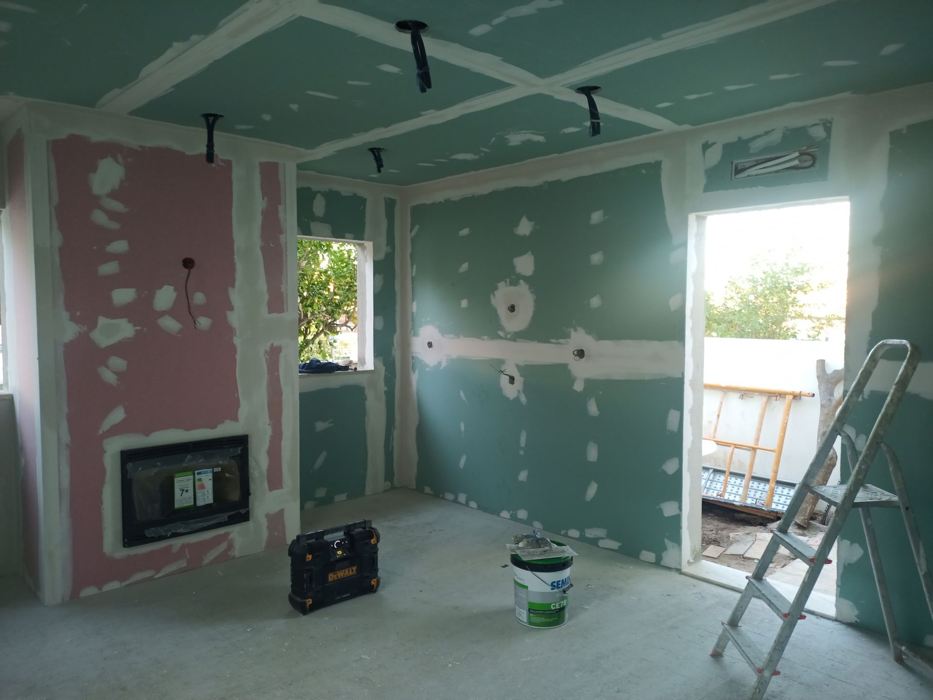Sala em construção com drywall verde e rosa, escada e ferramentas.