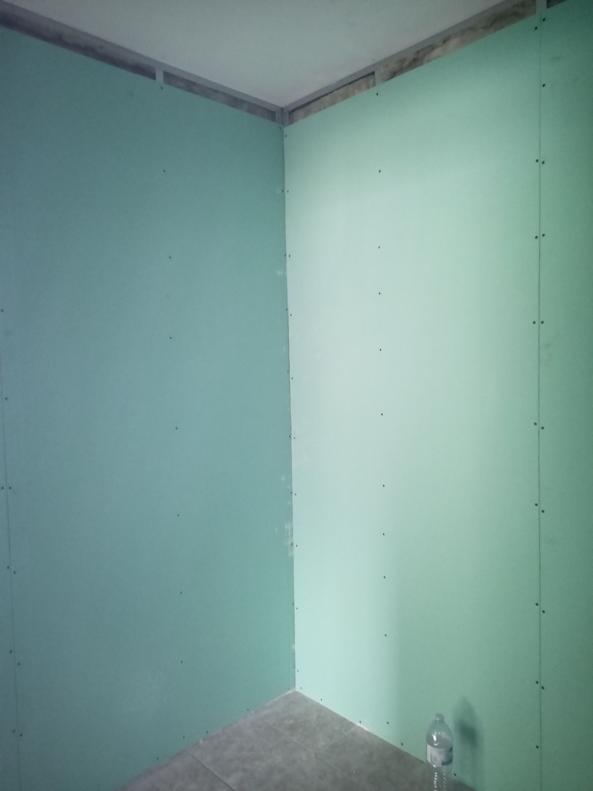Placa de gesso verde instalada em um canto da sala, pronta para o acabamento.