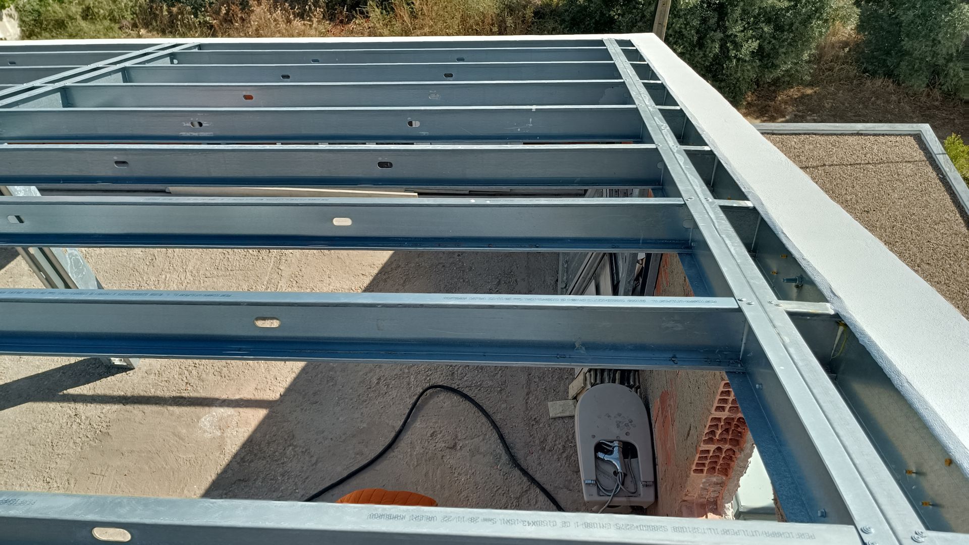 Estrutura metálica para telhado ou toldo, com vigas e suportes, ao ar livre em um dia ensolarado.