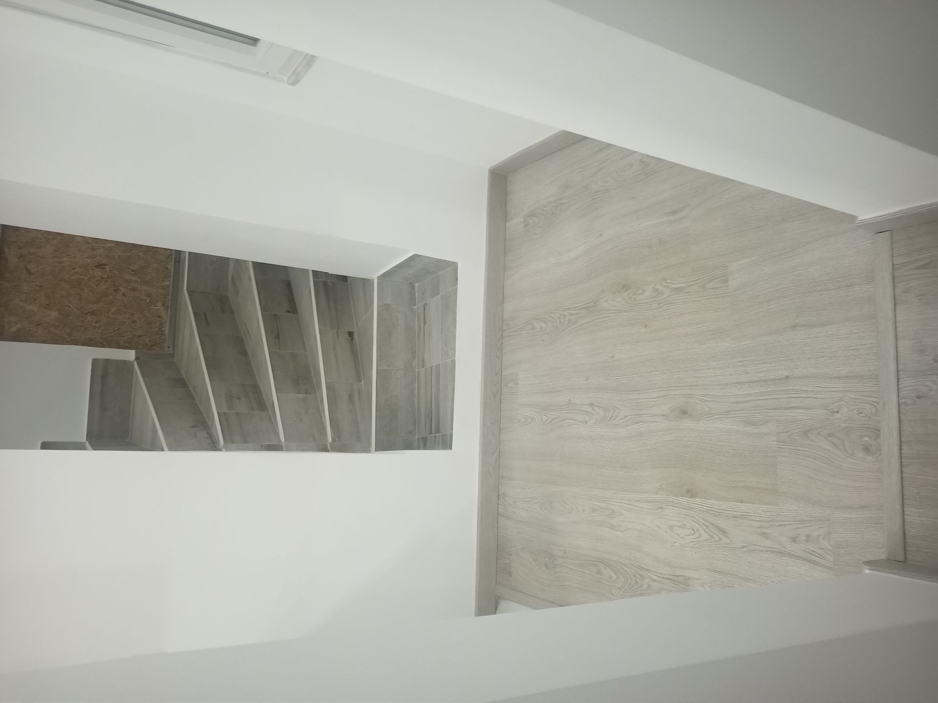 Escadaria com degraus de pedra cinza e painéis de parede combinando, vista de cima, cercada por paredes brancas.