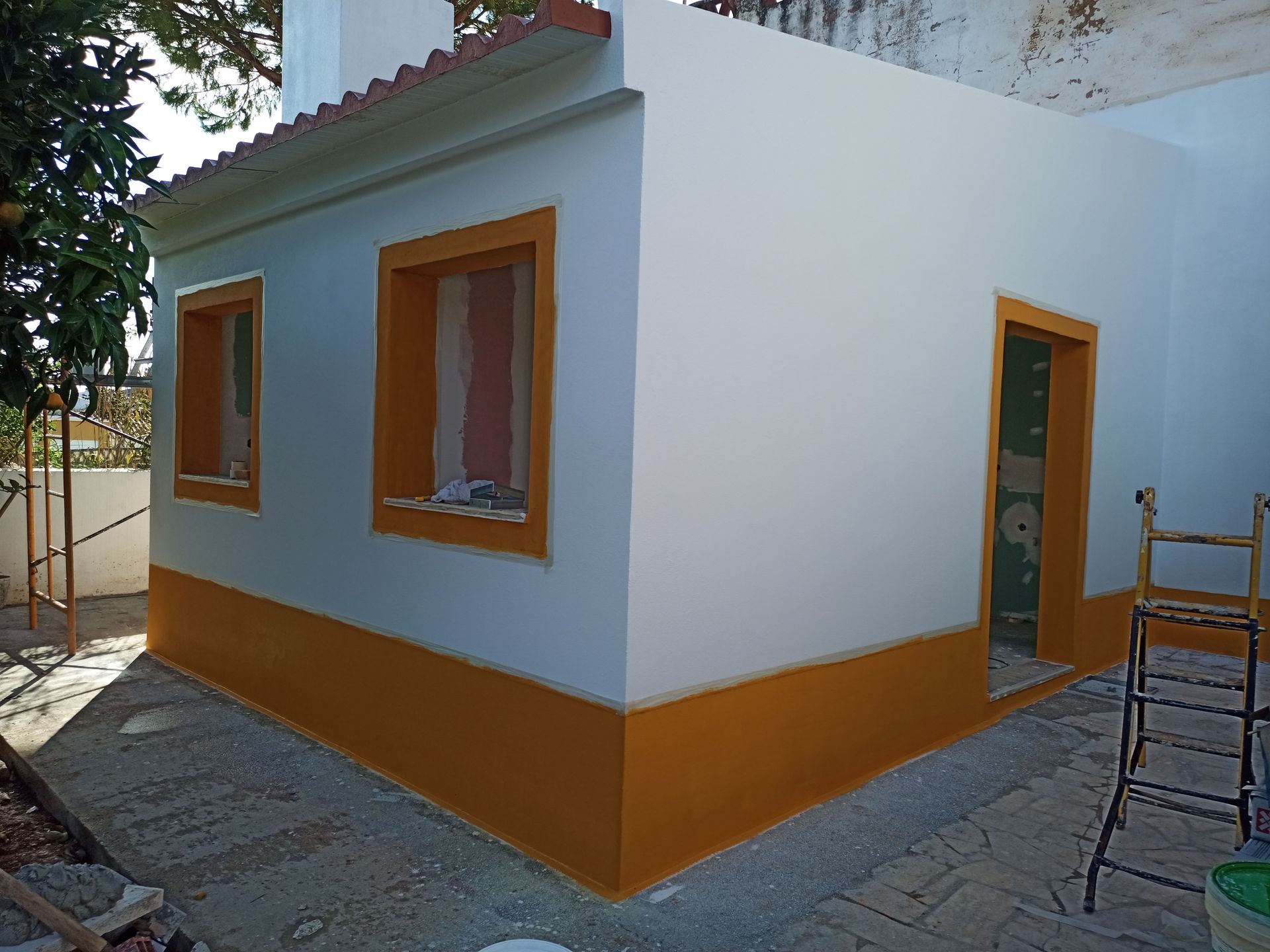 Canto exterior de um edifício, pintado de branco com detalhes em laranja ao redor das janelas e na base.