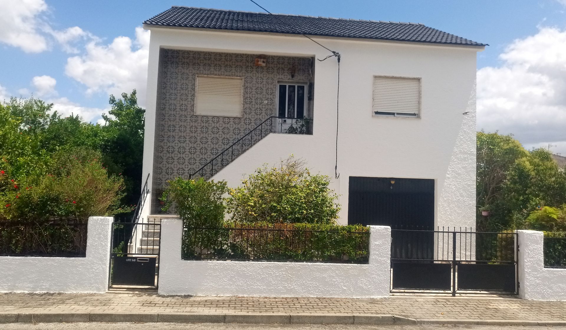 Casa branca de dois andares com porta de garagem preta, escadas que levam à porta da frente e cerca de ferro forjado.