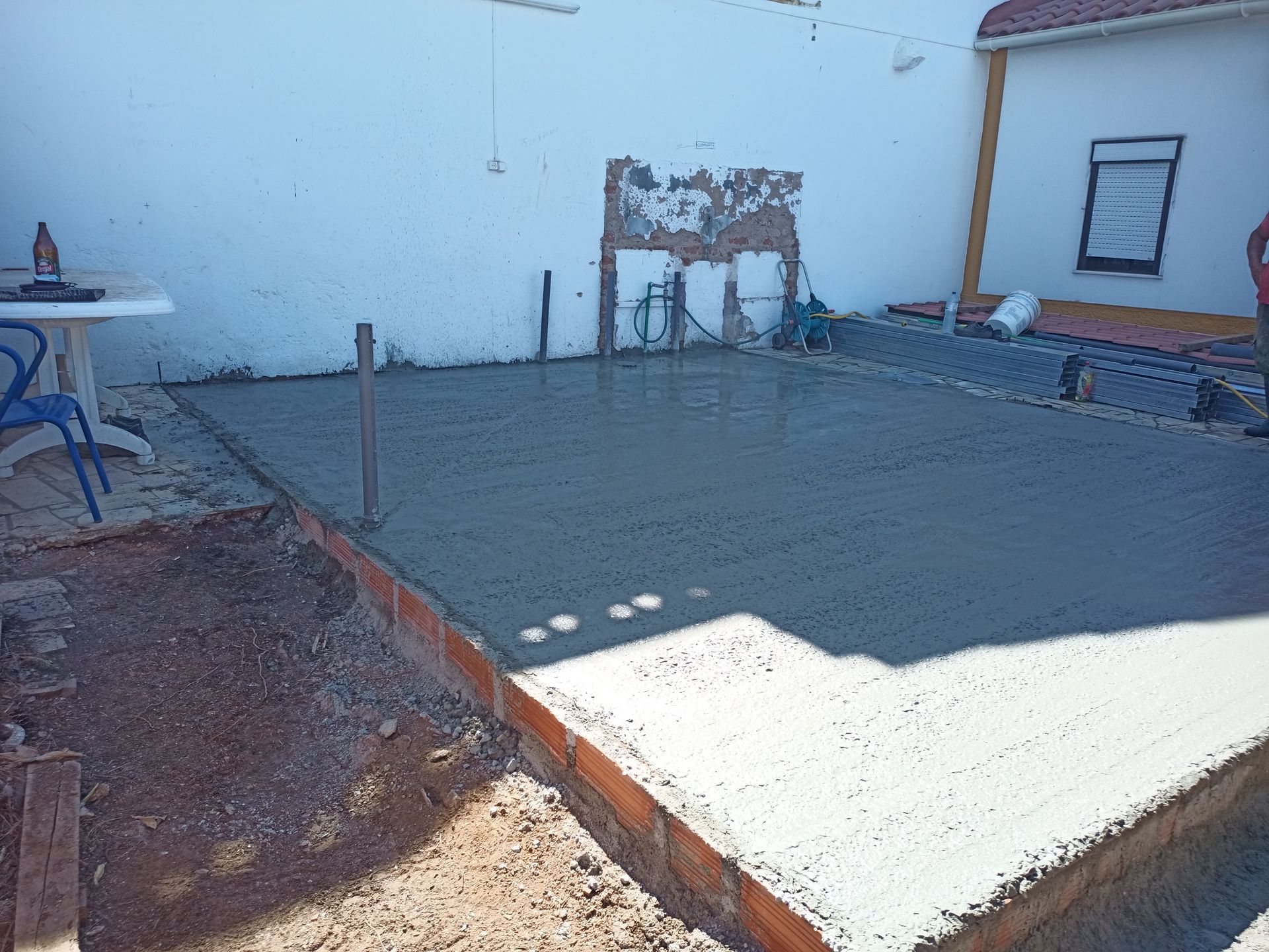 Pátio de concreto recém-construído cercado por borda de tijolos; paredes brancas ao fundo.