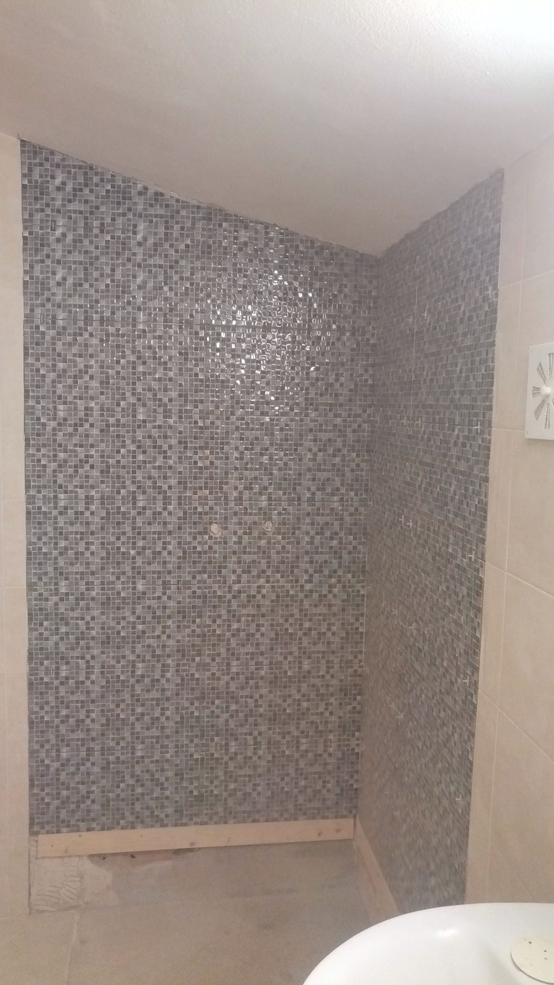 Chuveiro de canto com azulejos de mosaico cinza e paredes bege.