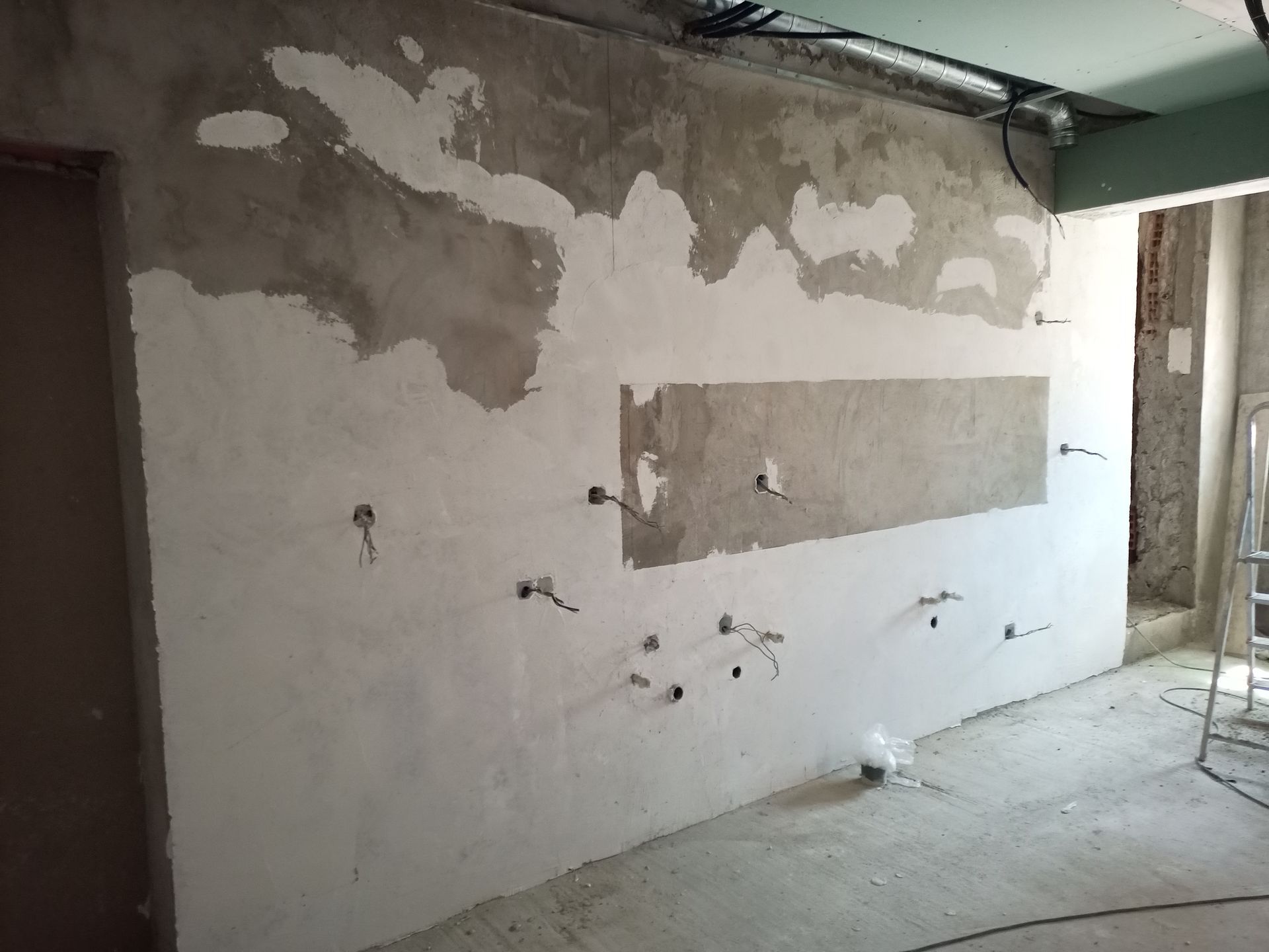 Parede interna com fiação elétrica e reboco inacabado da época da construção. Uma porta e o vão da porta são visíveis.