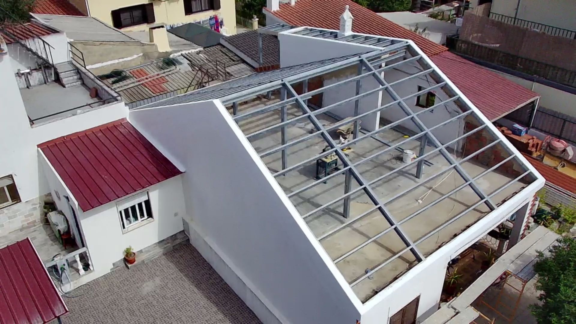 Operários em um telhado em construção, com estrutura metálica e telhas vermelhas visíveis.