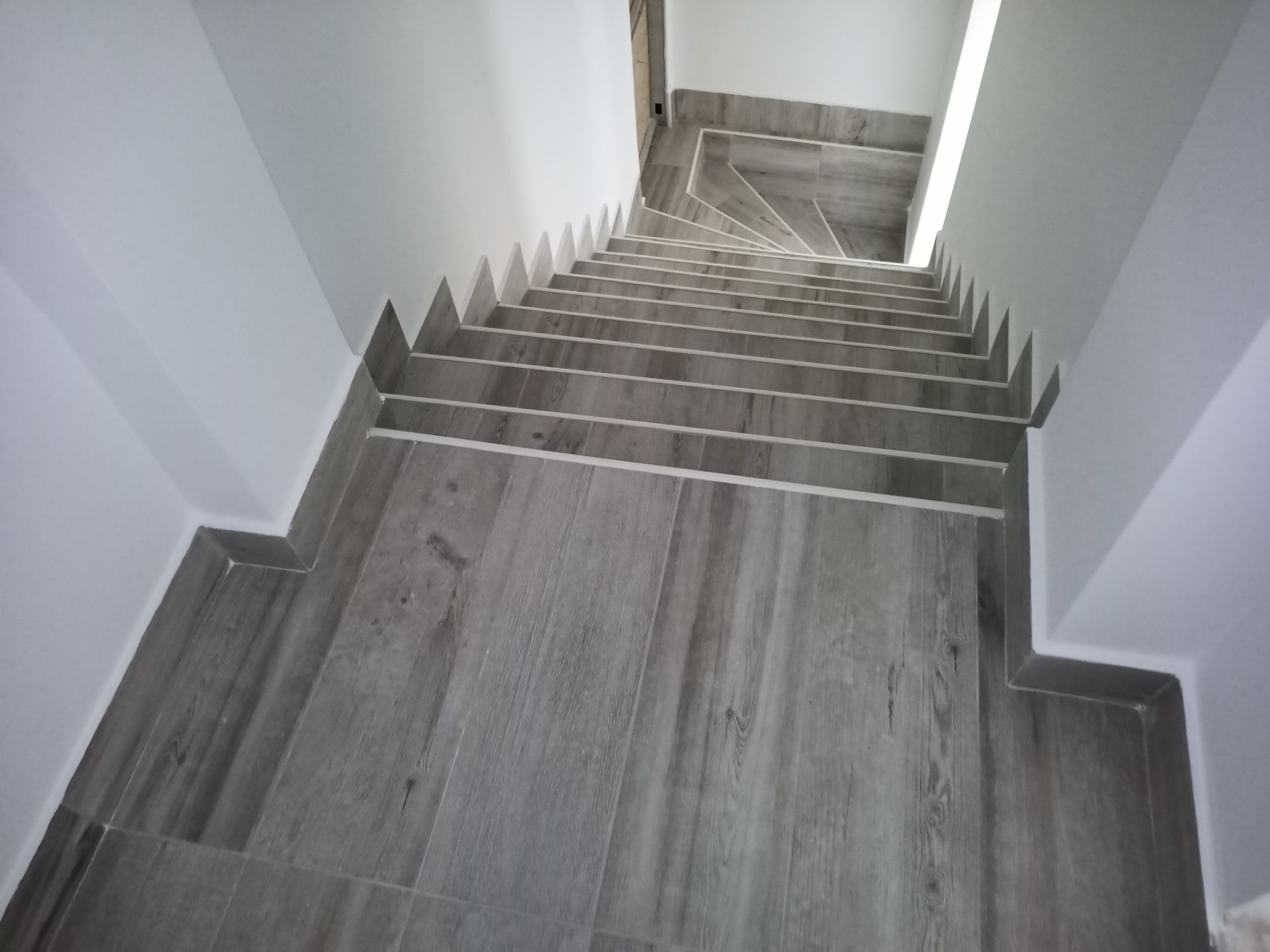 Vista de uma escadaria cinza com aparência de madeira e paredes brancas em ambos os lados.