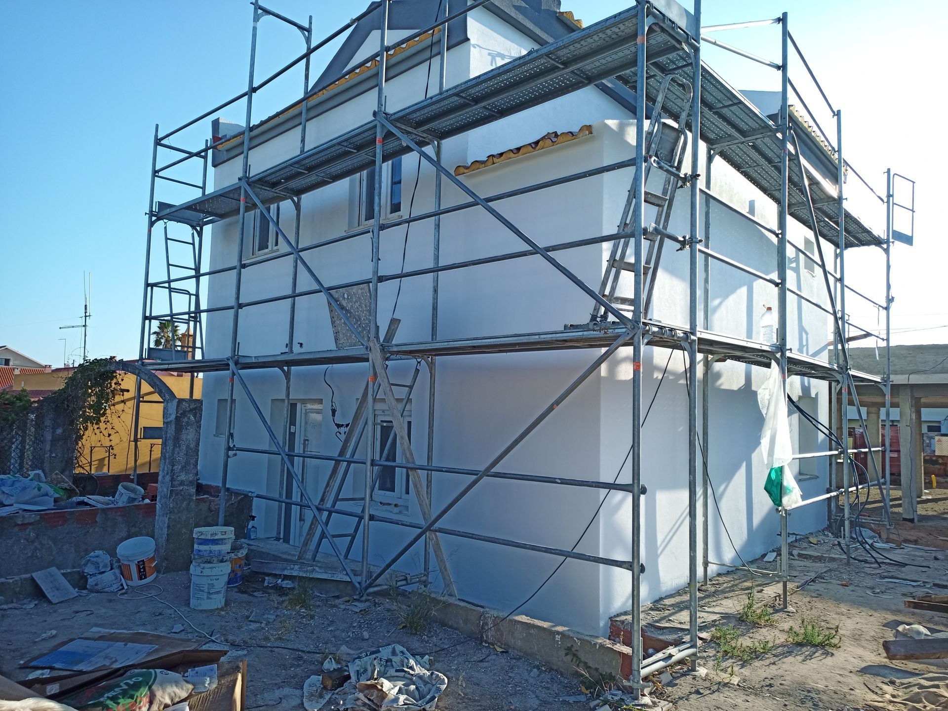 Andaimes cercam um prédio branco de dois andares em construção; a parte externa está danificada.