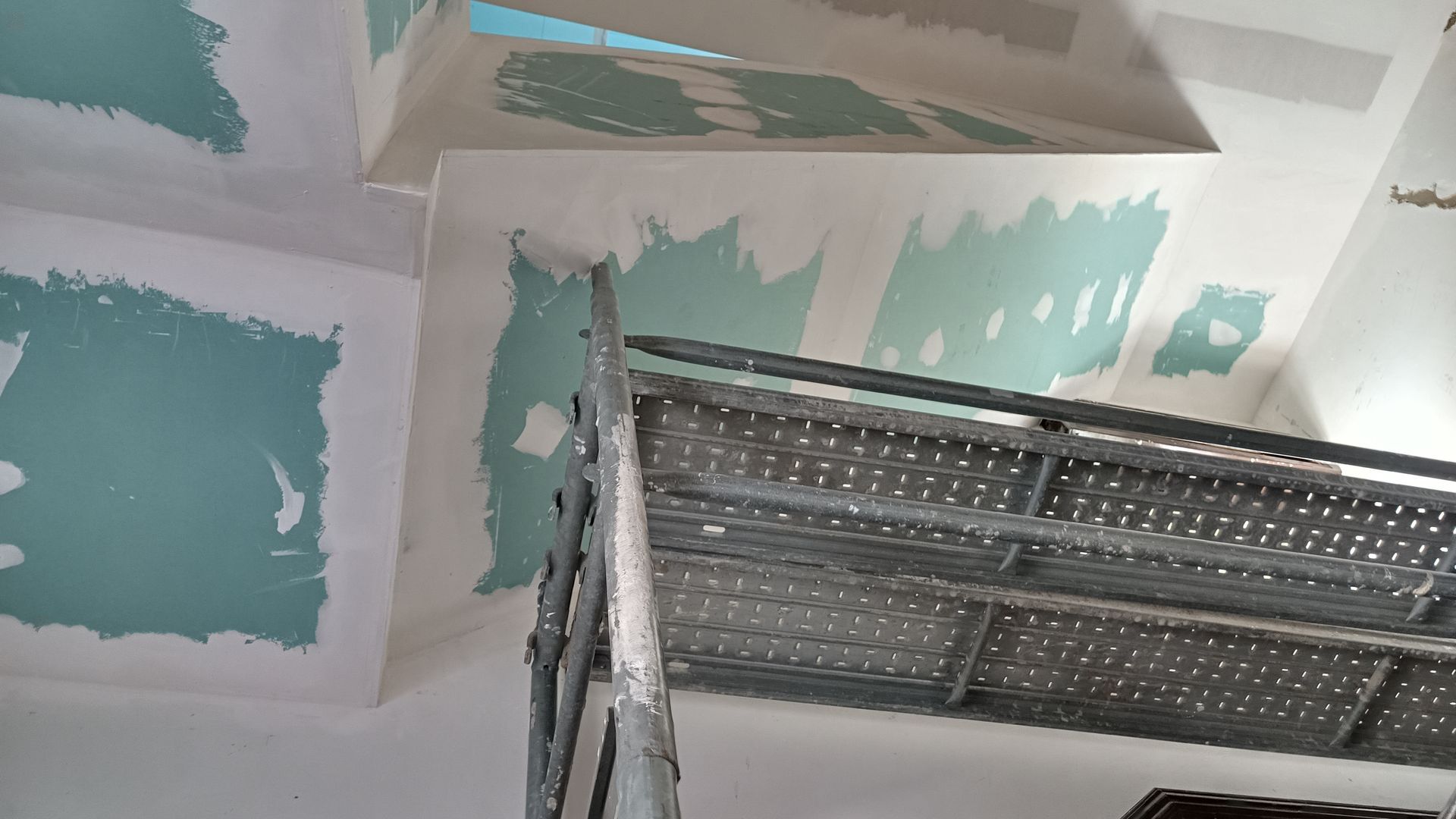 Teto com manchas de material turquesa, andaimes em primeiro plano.