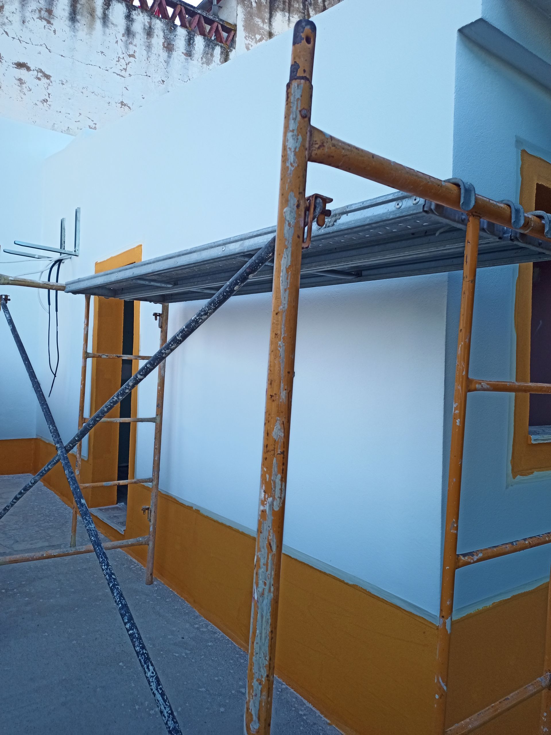 Andaimes encostados em um prédio pintado de azul claro e amarelo.