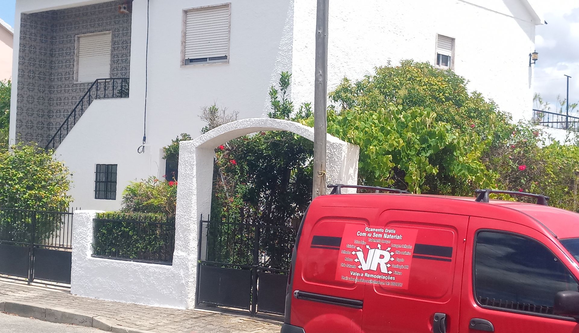 Prédio de estuque branco com uma van vermelha estacionada em frente a um portão e arco de ferro forjado.