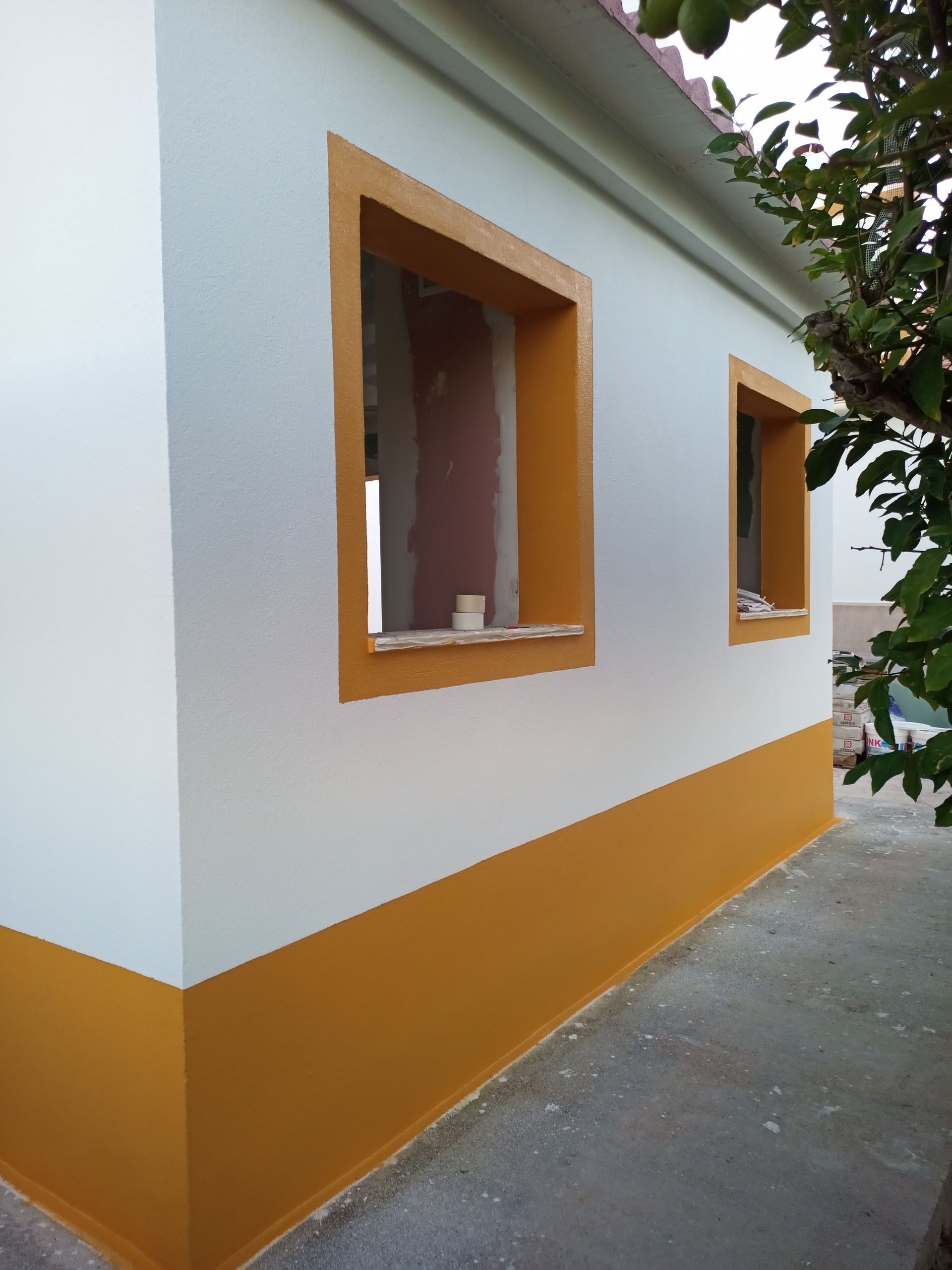 Exterior do edifício com paredes pintadas de branco e amarelo, duas janelas com contorno amarelo.