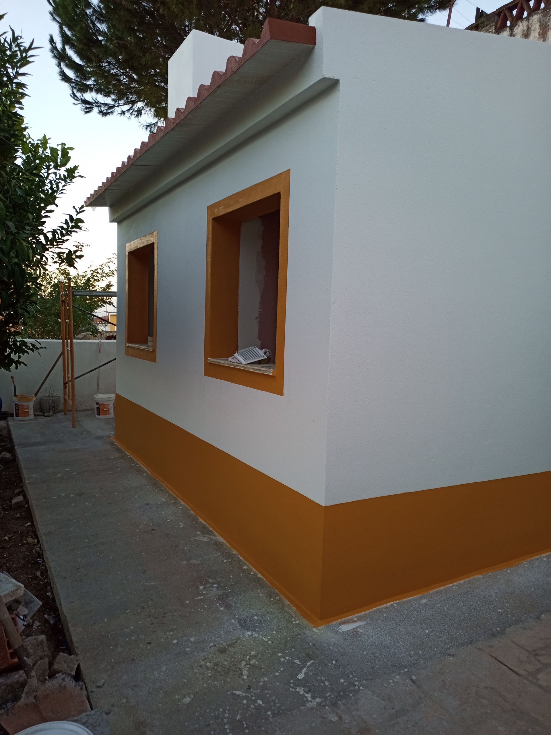 Exterior branco e amarelo de um pequeno edifício. Detalhes em laranja emolduram as janelas e a base.