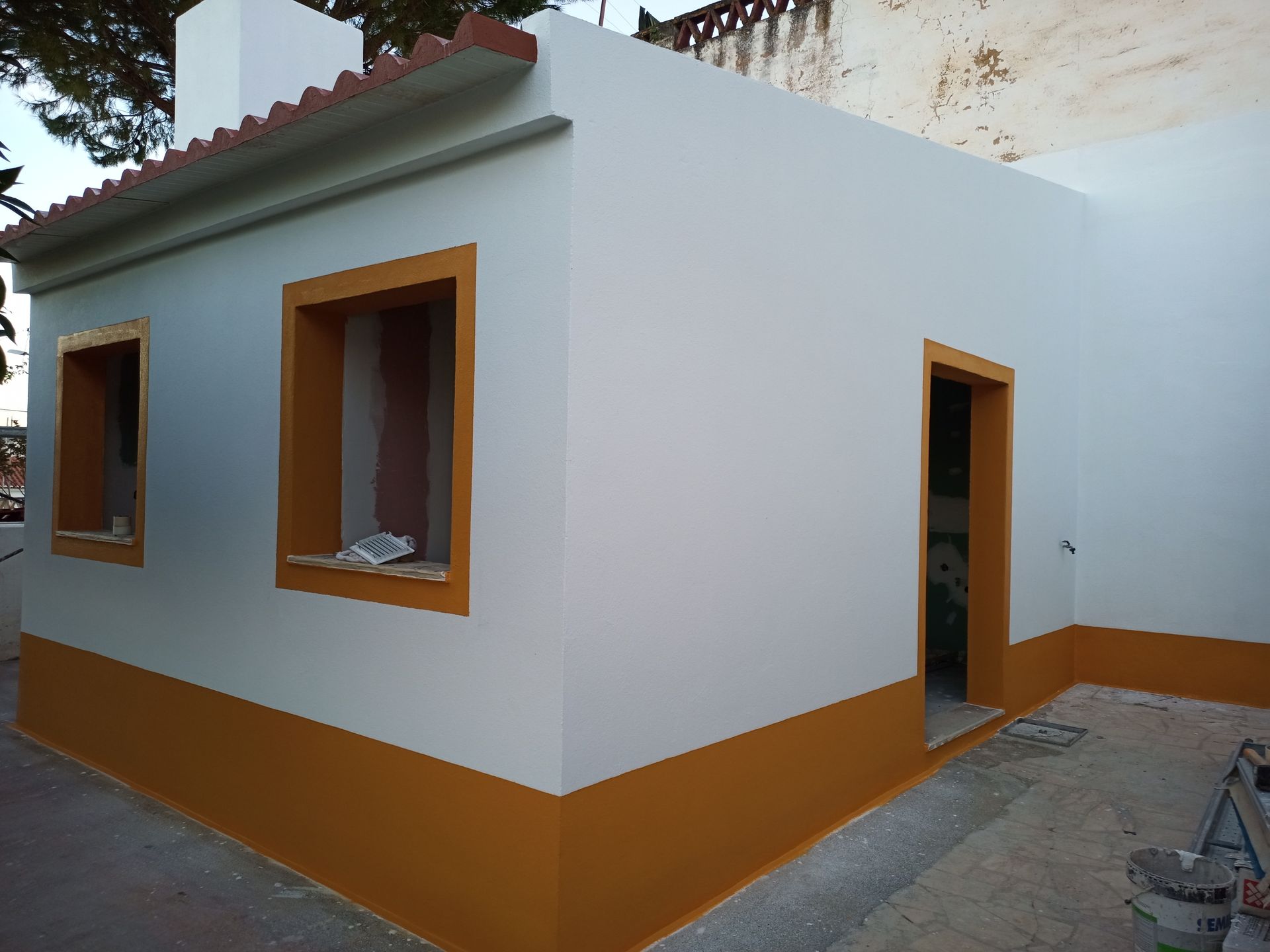 Prédio branco com detalhes e telhas laranja, duas janelas e uma porta aberta.