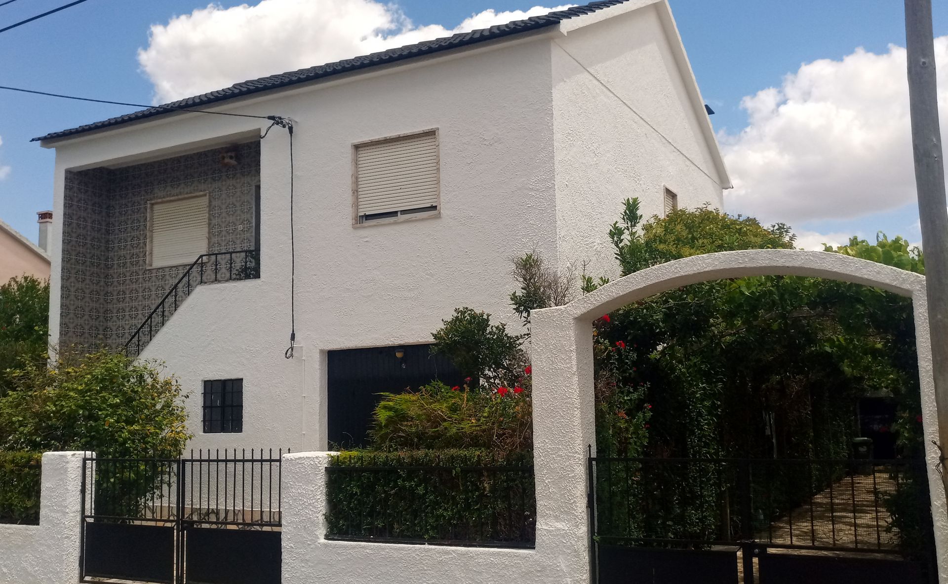 Casa branca de dois andares com detalhes em preto, uma pequena cerca preta e um arco coberto de folhagem verde.