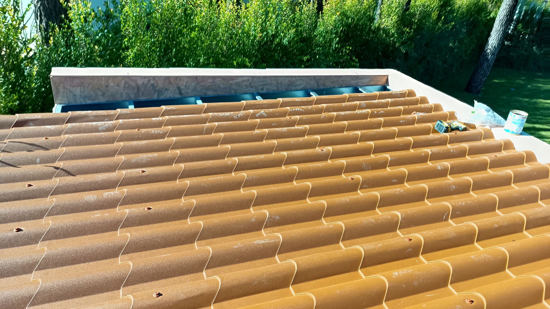 Telhado de telha marrom com borda clara e vegetação ao fundo.