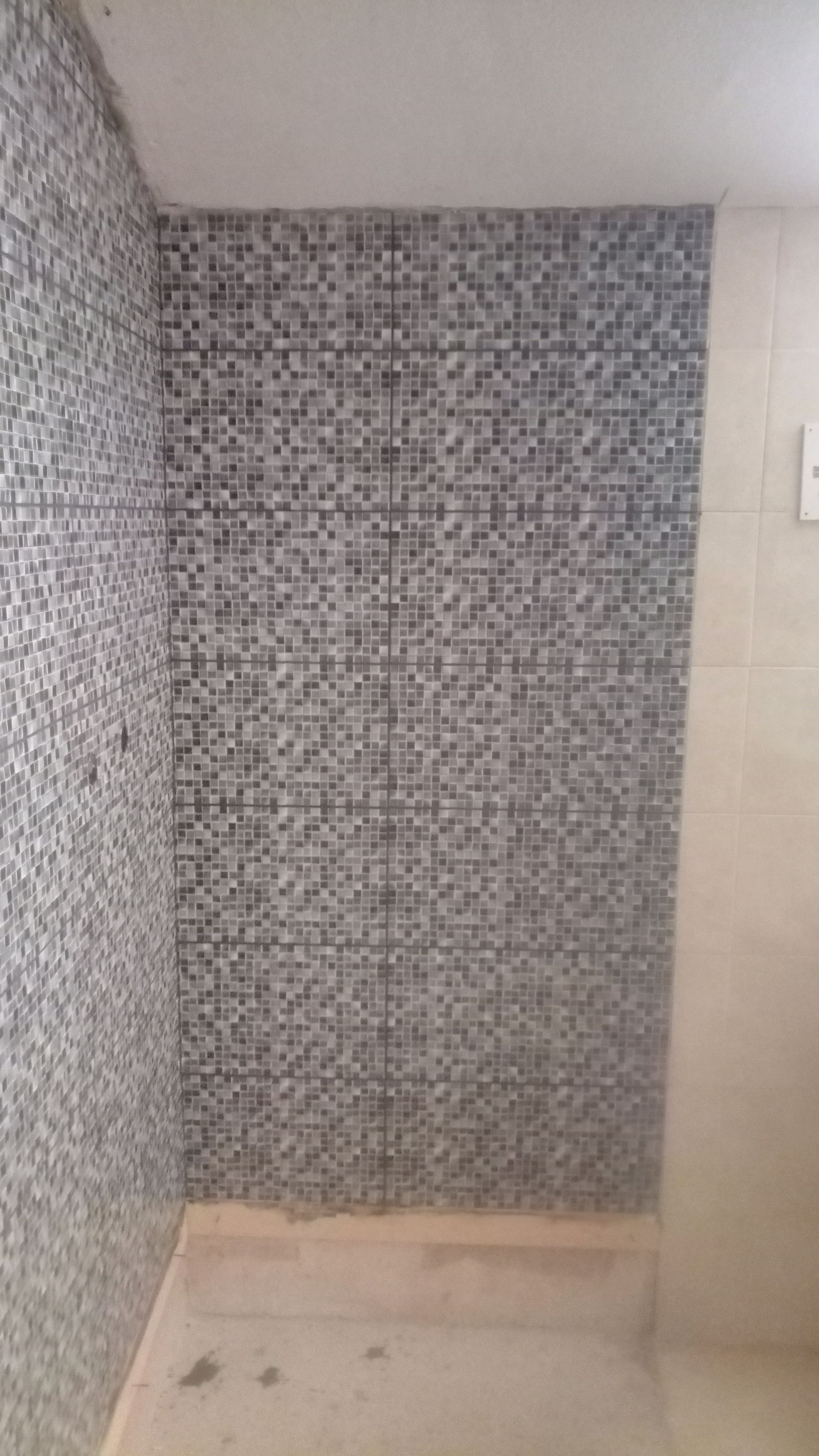 Canto de banheiro com paredes revestidas com azulejos em mosaico e paredes circundantes em bege claro.