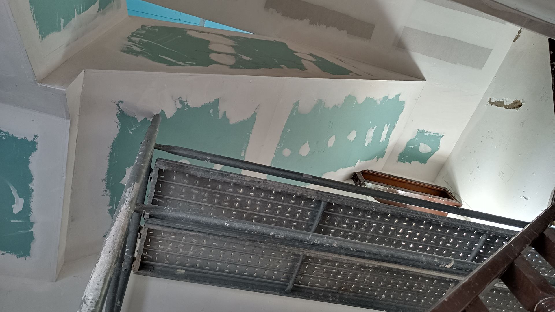 Teto e paredes internas em construção, com massa de remendo verde visível; andaimes presentes.
