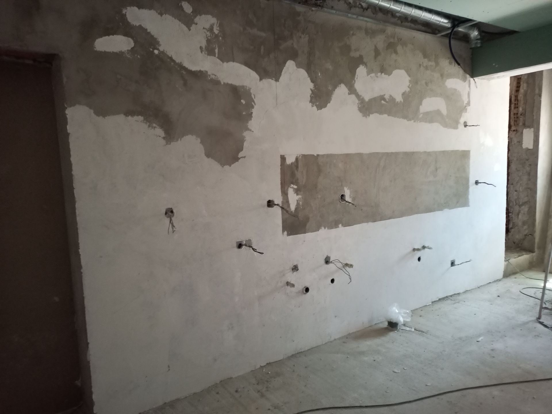 Parede em construção com fiação elétrica exposta, mostrando remendos e um retângulo embutido.