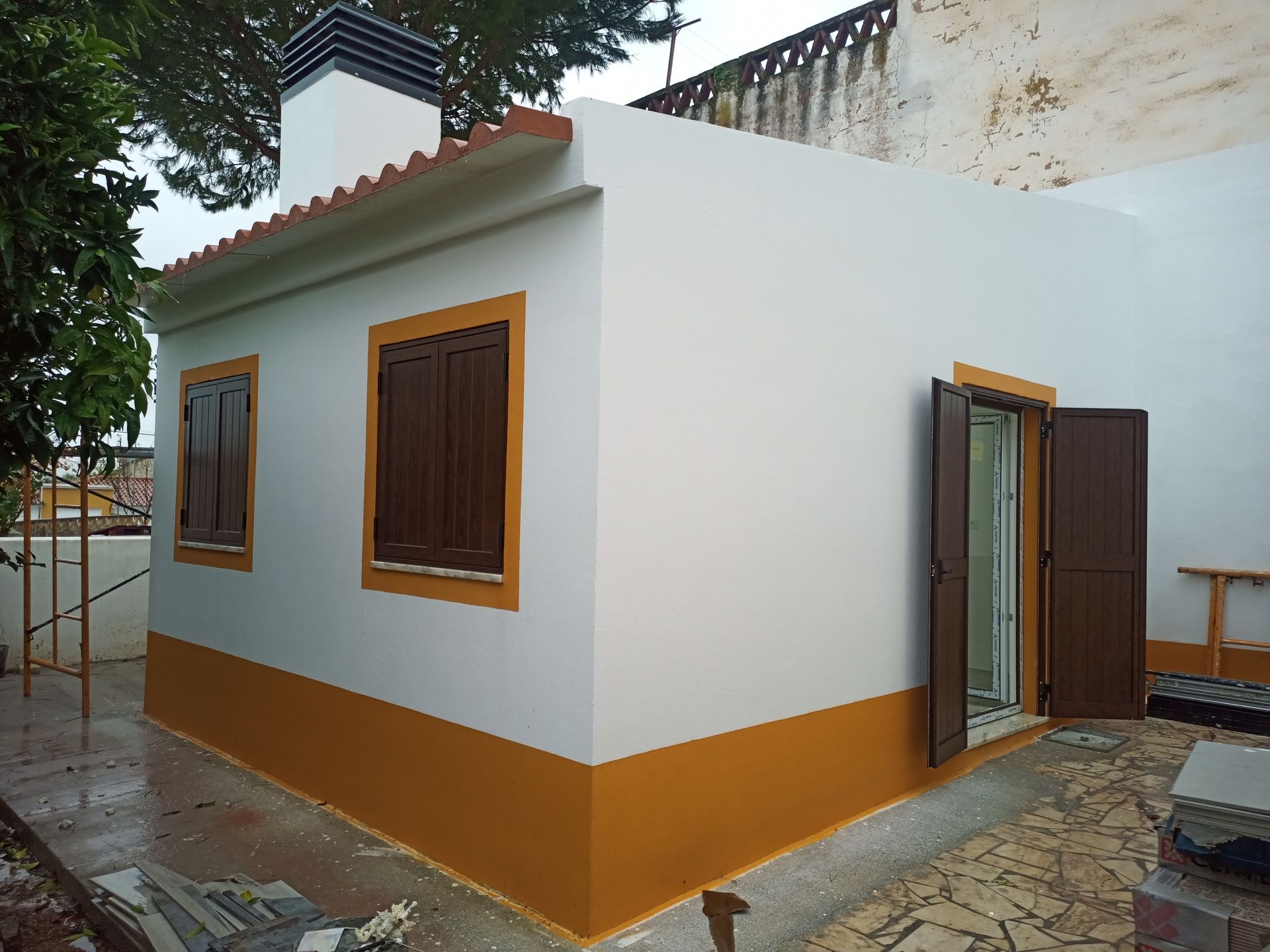 Prédio branco com detalhes e venezianas marrons, base laranja. Chaminé visível.