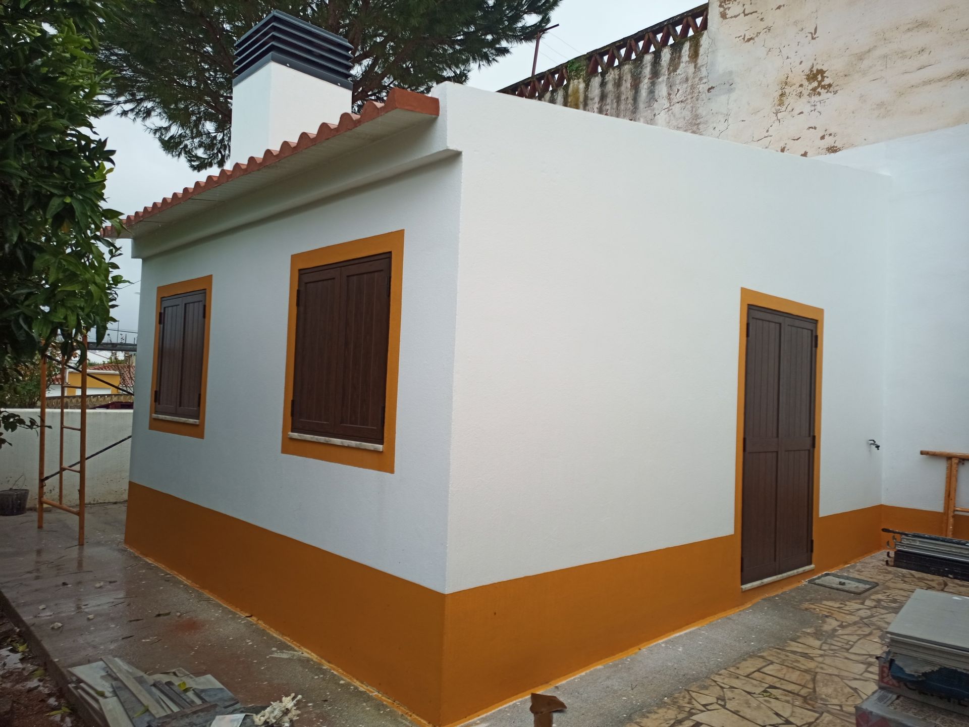 Pequeno prédio branco com detalhes em marrom, venezianas e porta, base e telhado em laranja.