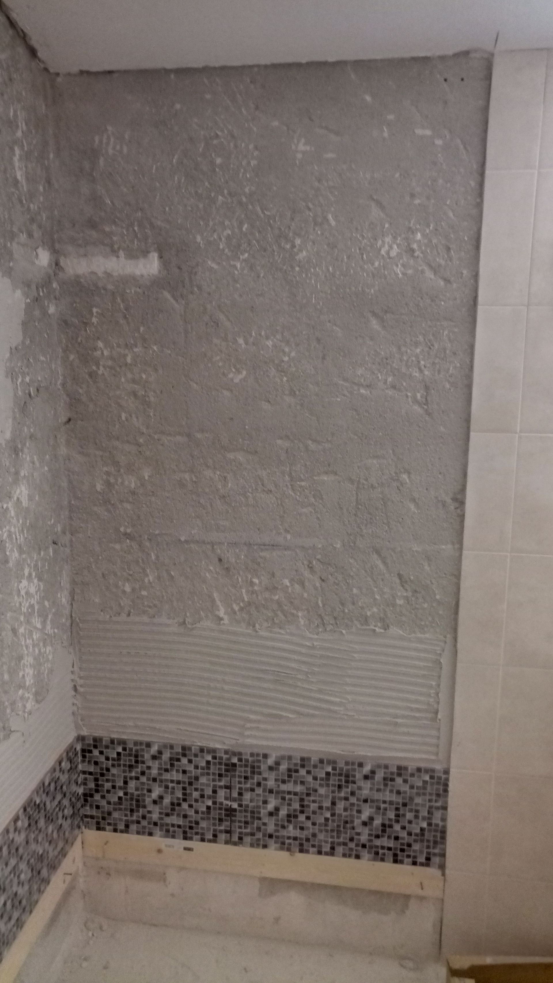 Parede do banheiro com azulejos variados em tons de cinza e com padrões, construção inacabada.