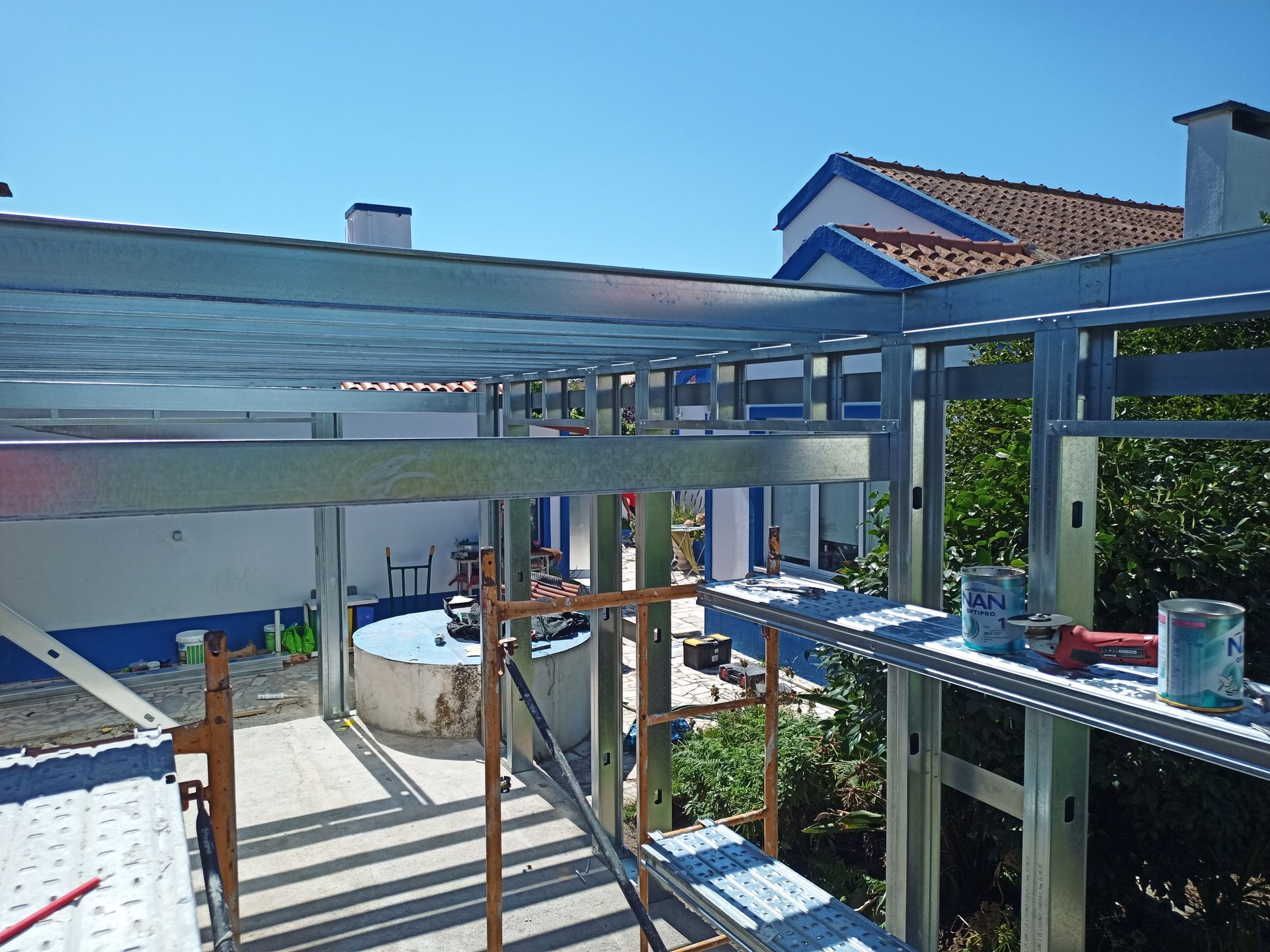 Canteiro de obras: Estrutura metálica com andaimes, vista de uma casa.