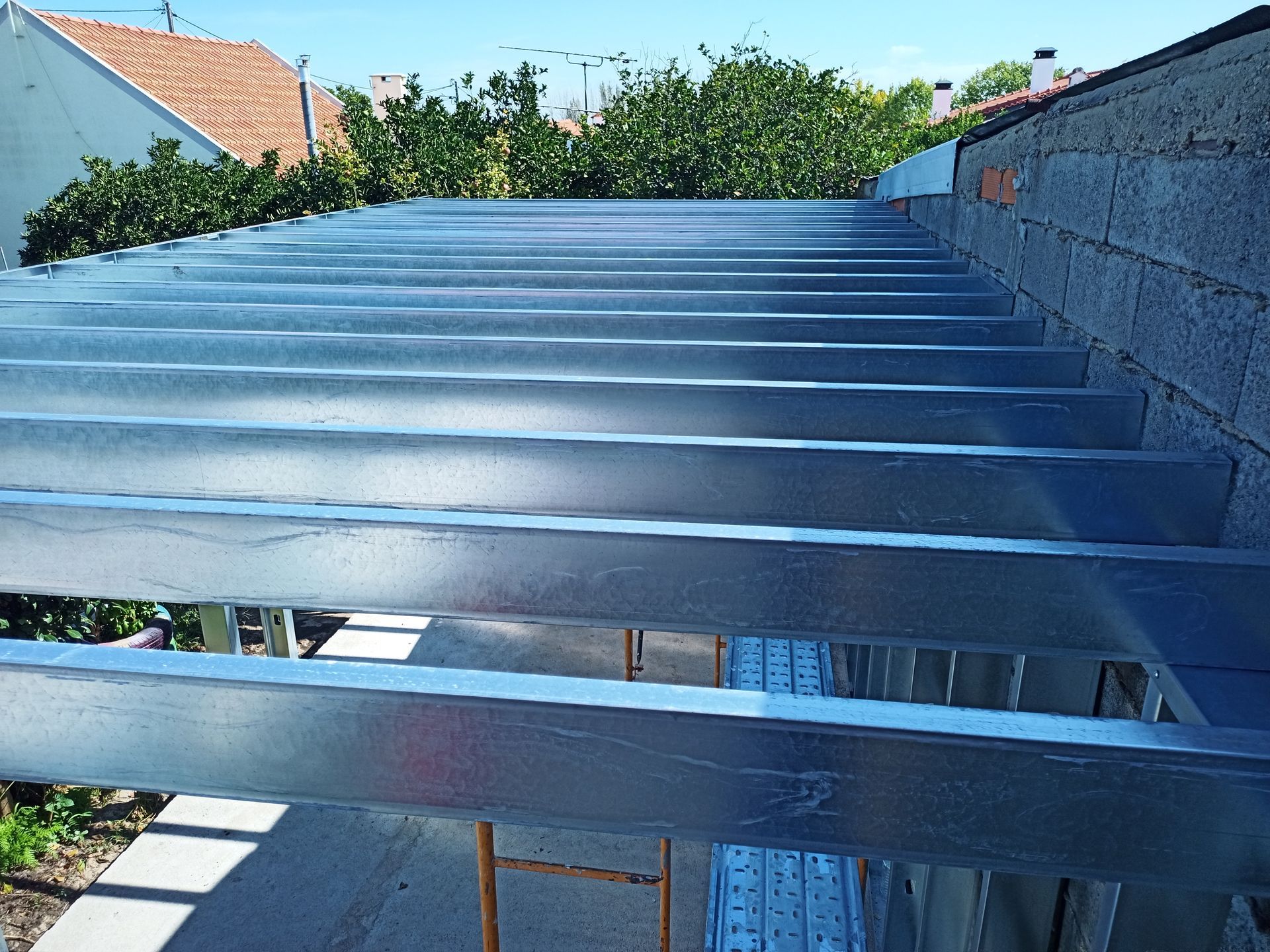 Vigas metálicas formando a estrutura do telhado, com o céu azul visível acima.