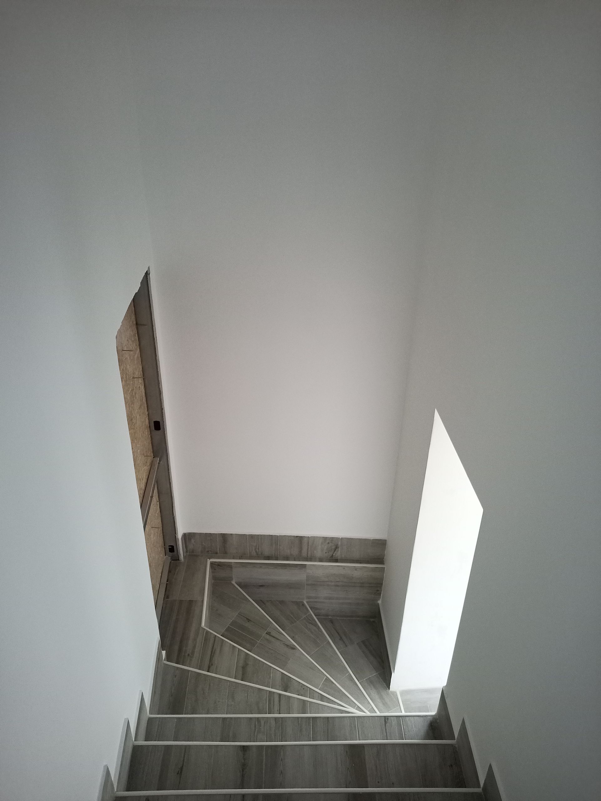 Escadaria com degraus cinzentos e paredes brancas; vista do topo.