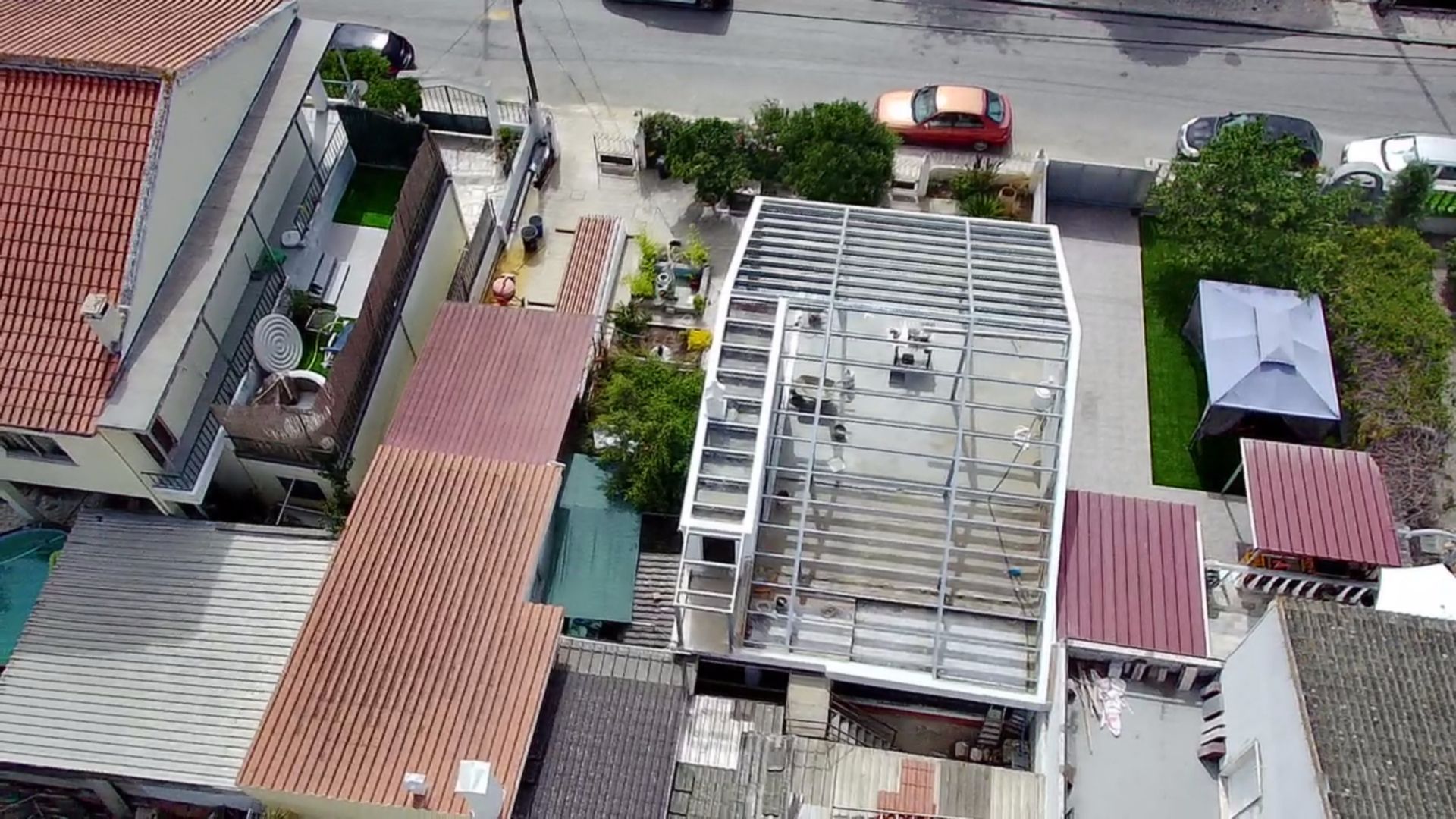 Vista aérea de um edifício branco de vários andares com o telhado parcialmente construído, situado em meio a outros edifícios e à rua.
