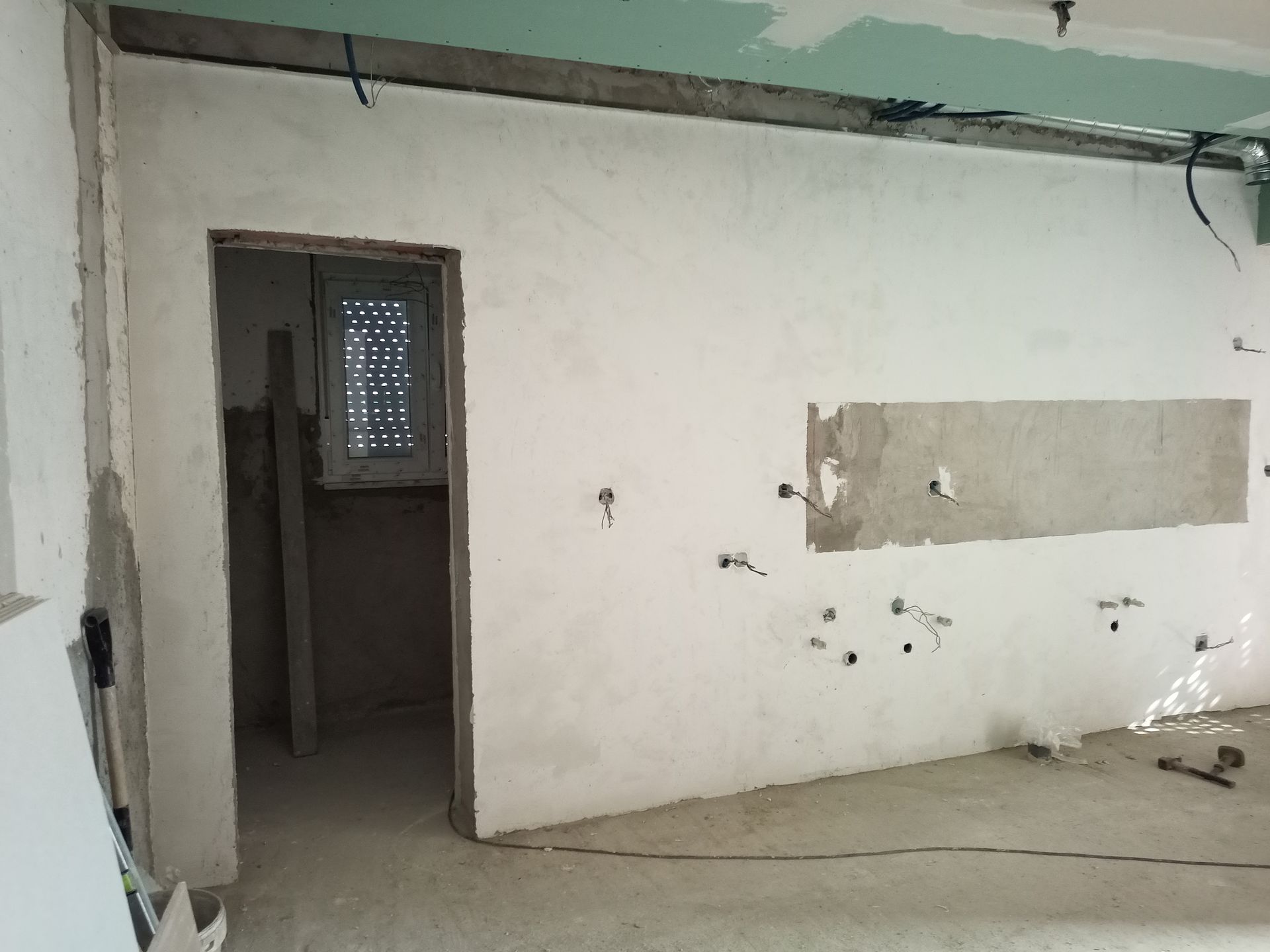 Reforma interna em andamento: porta de entrada, parede remendada, fiação elétrica, teto e piso inacabados.