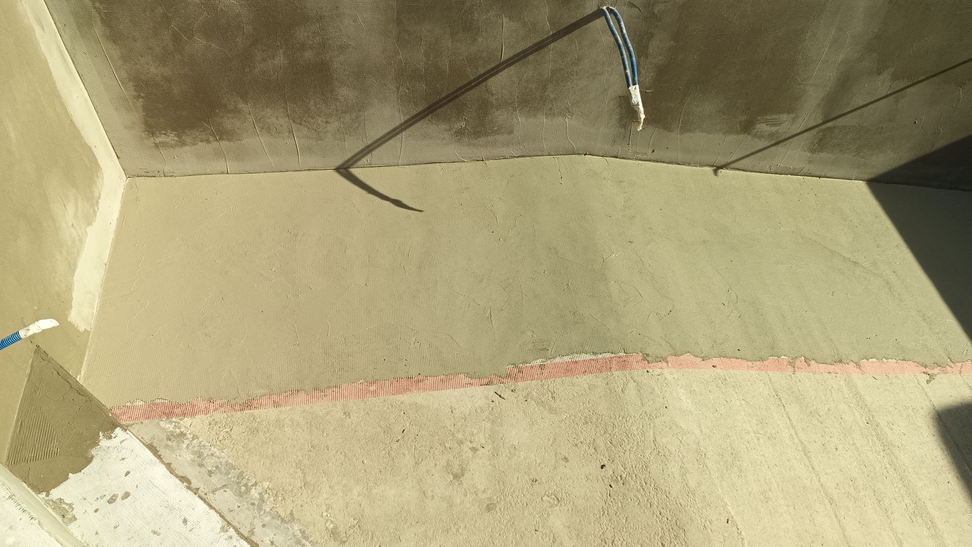 Parede interna em construção; estuque, tela e conduíte elétrico visíveis.