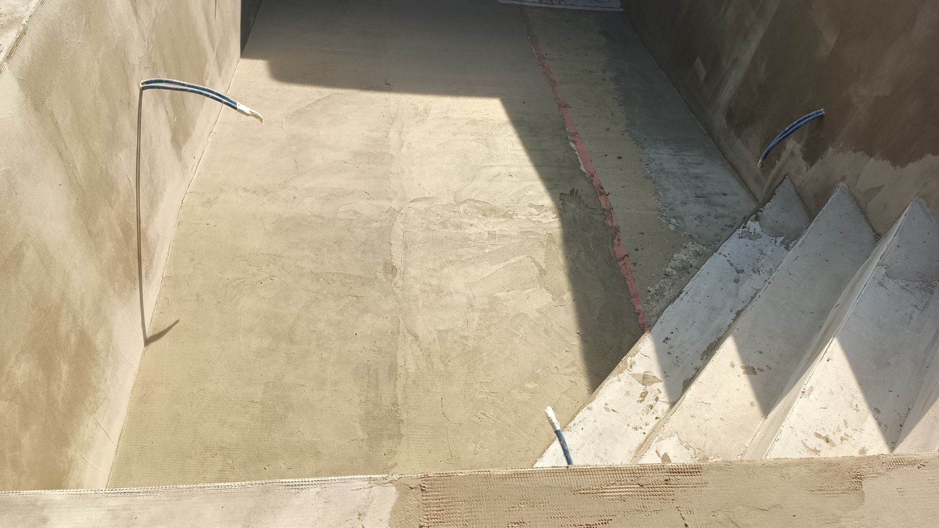 Piscina de concreto vazia com escadas. A luz do sol projeta sombras.