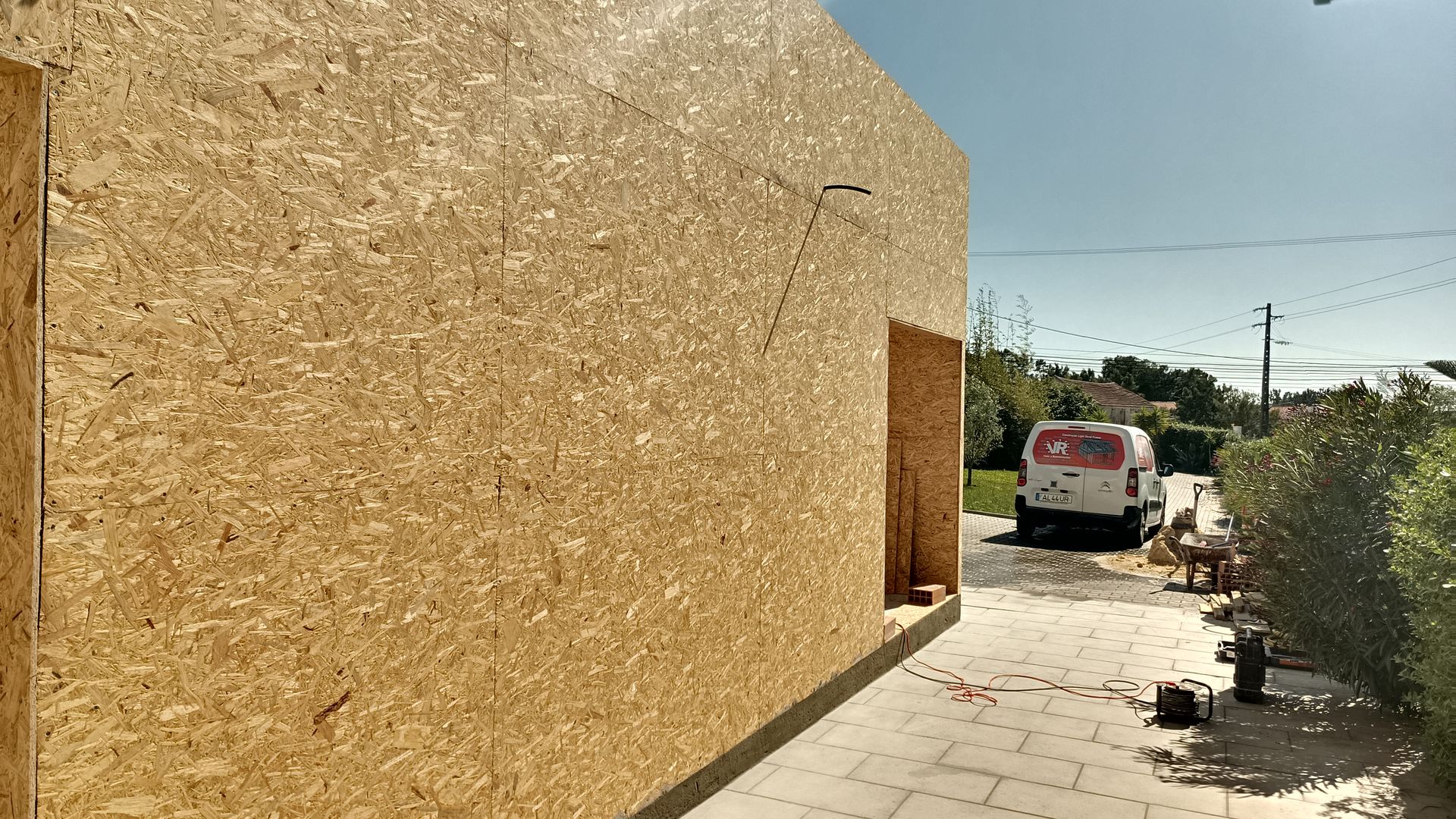 Exterior de um prédio em construção, paredes de placas OSB. Uma van estacionada nas proximidades.