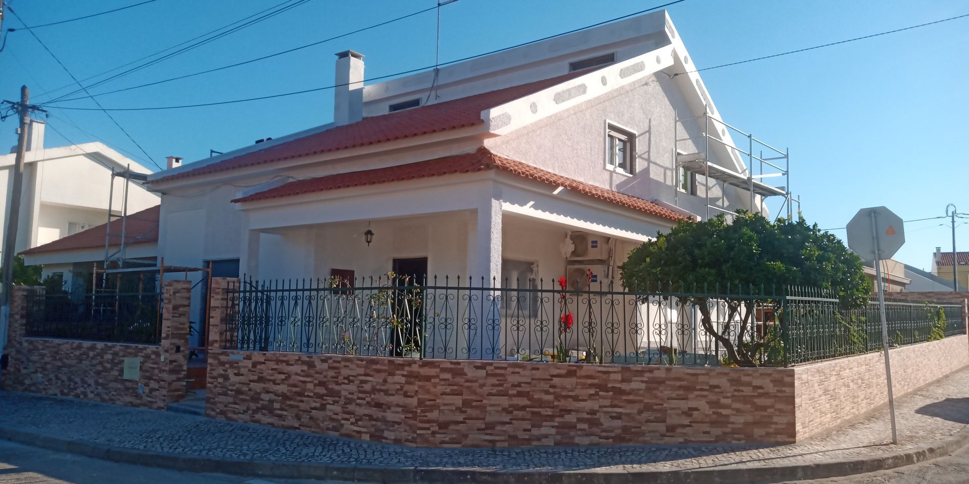 Casa com telhado de telha vermelha, paredes brancas e muro de tijolos em um dia ensolarado.