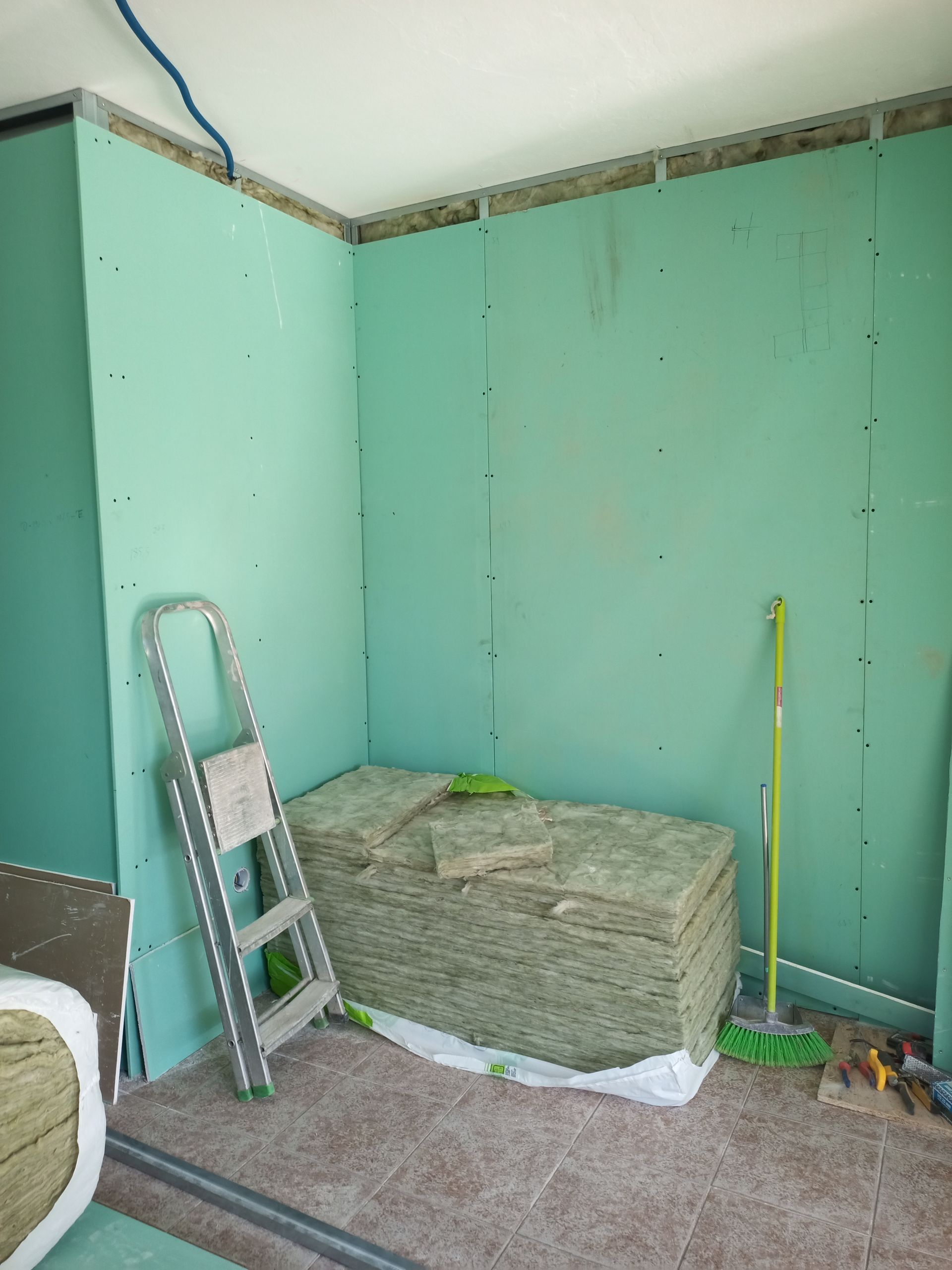 Canteiro de obras com drywall verde, isolamento e uma escada.