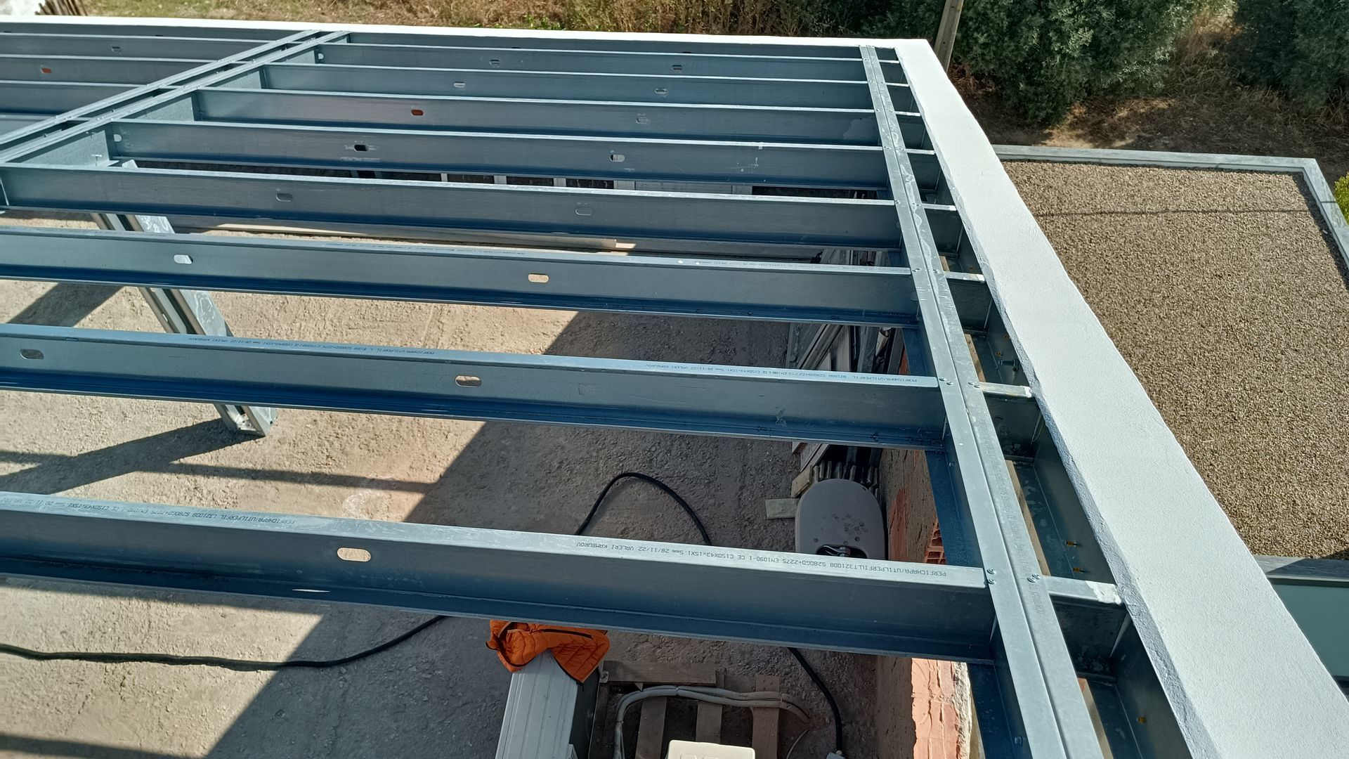 Estrutura metálica para cobertura, com vigas horizontais e borda. Tons de cinza e azul.