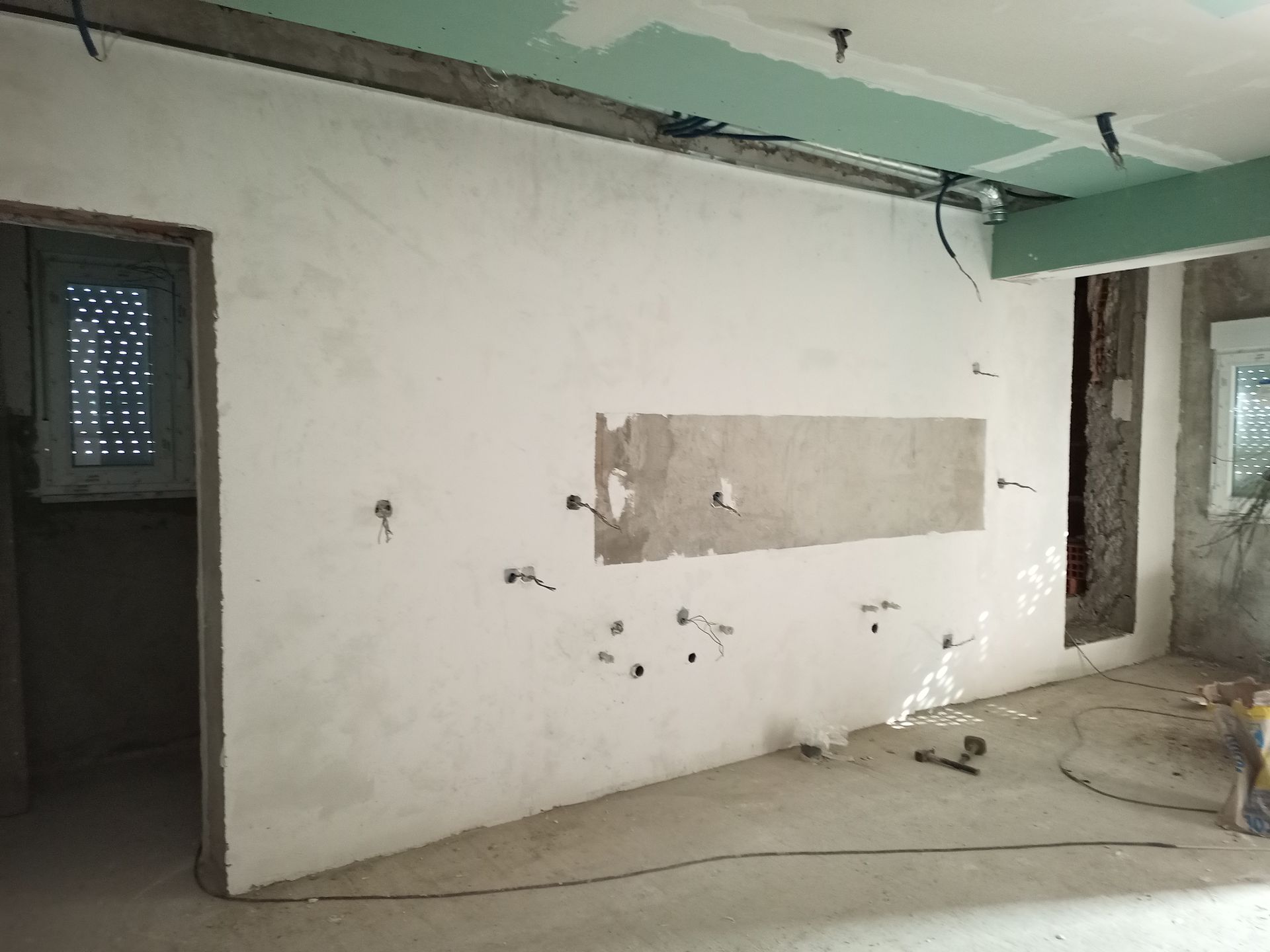 Quarto interior em construção, paredes de gesso com fiação elétrica exposta, porta e teto inacabado.