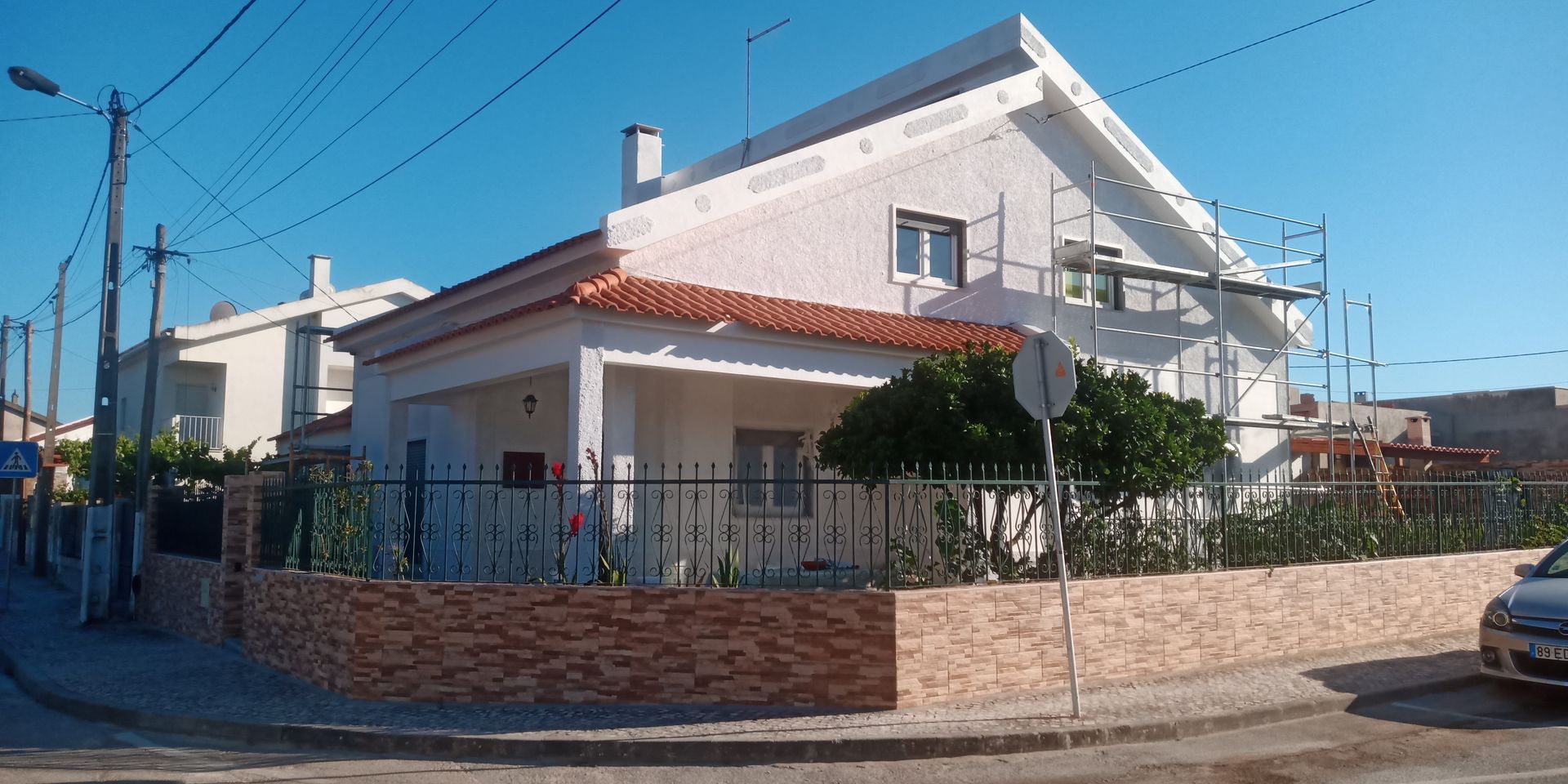 Uma casa branca de dois andares com andaimes, telhado de telha vermelha e parede de tijolos em um dia ensolarado.