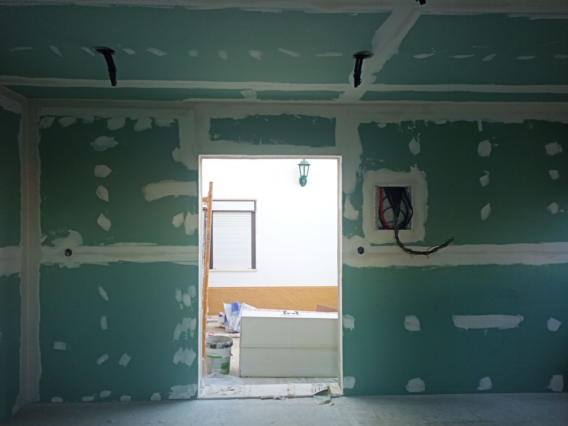 Interior de um cômodo em construção com drywall verde, fita adesiva branca e porta aberta.