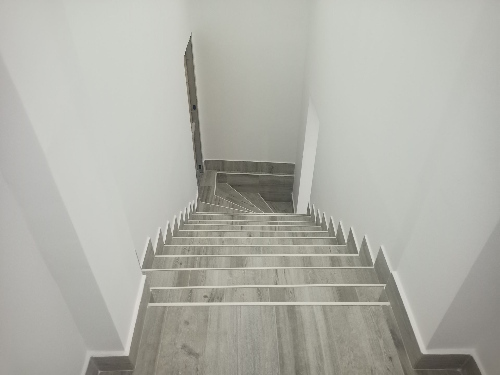 Escada vista de cima, descendo entre paredes brancas. Degraus cinzentos com bordas brancas.