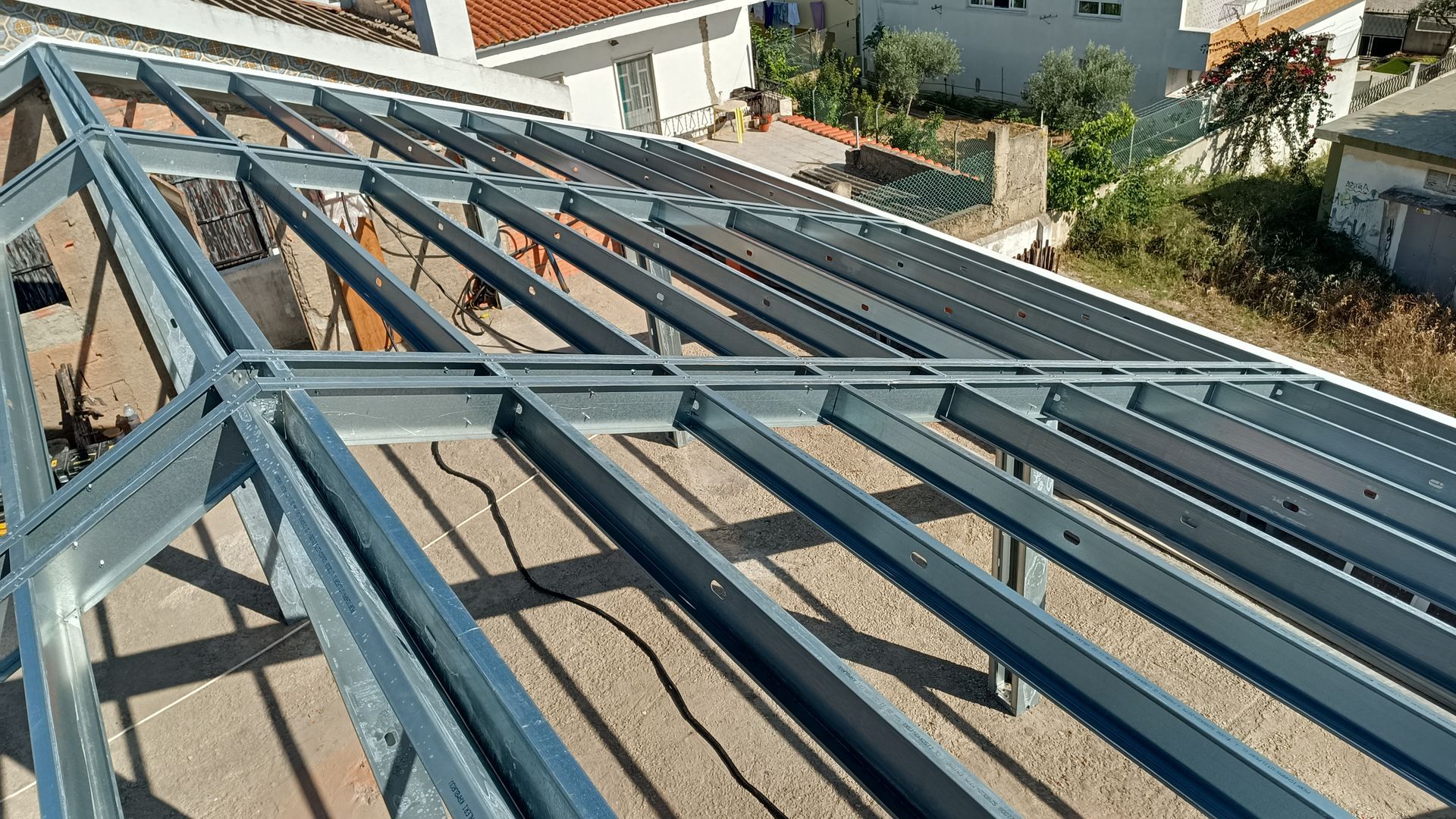 Estrutura metálica de um telhado em construção, na parte externa de um edifício, com múltiplas vigas.