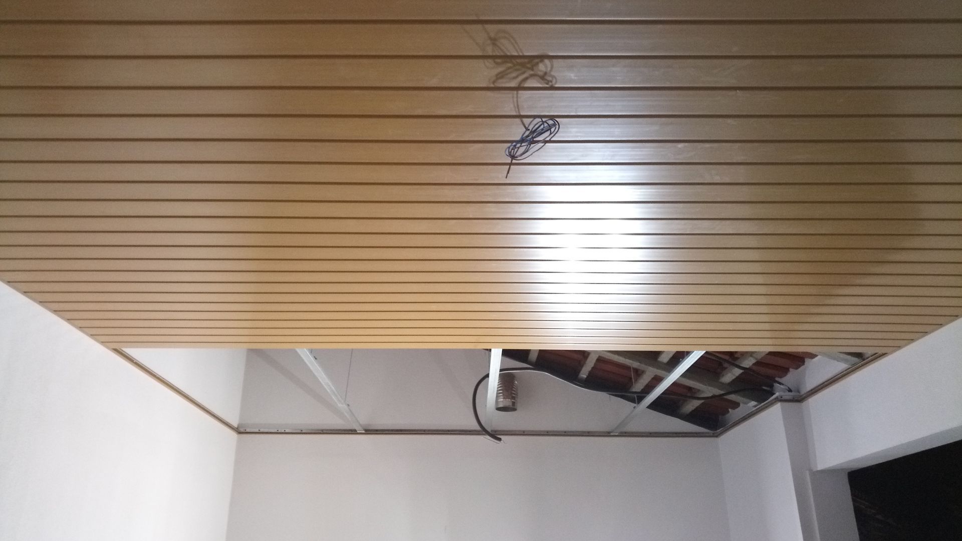 Teto com painéis de madeira; parte do teto exposta mostrando a fiação elétrica e as estruturas de suporte.