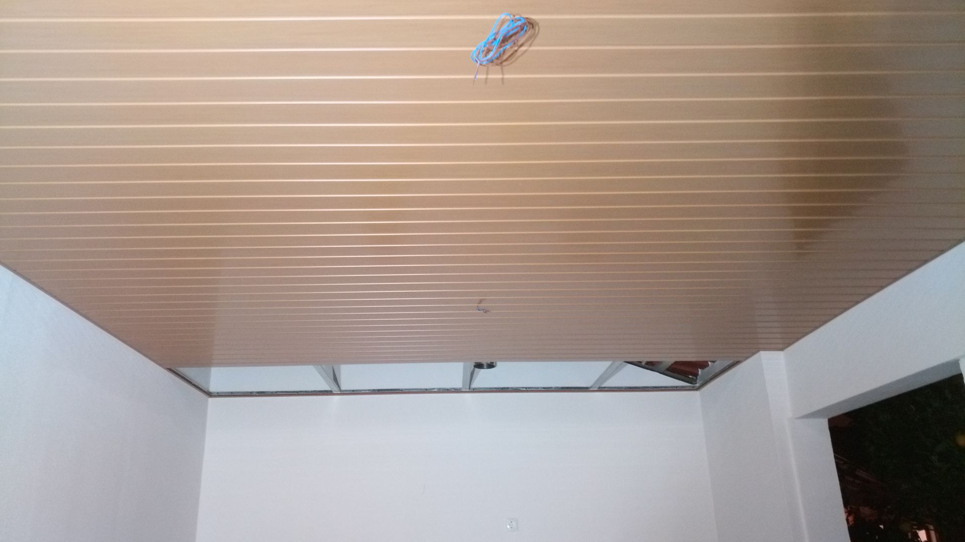 Teto com painéis marrons e estrutura metálica aparente, paredes brancas.