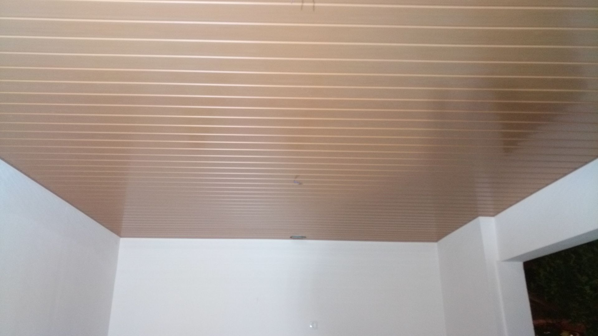 Teto marrom com ranhuras, paredes brancas e uma porta.