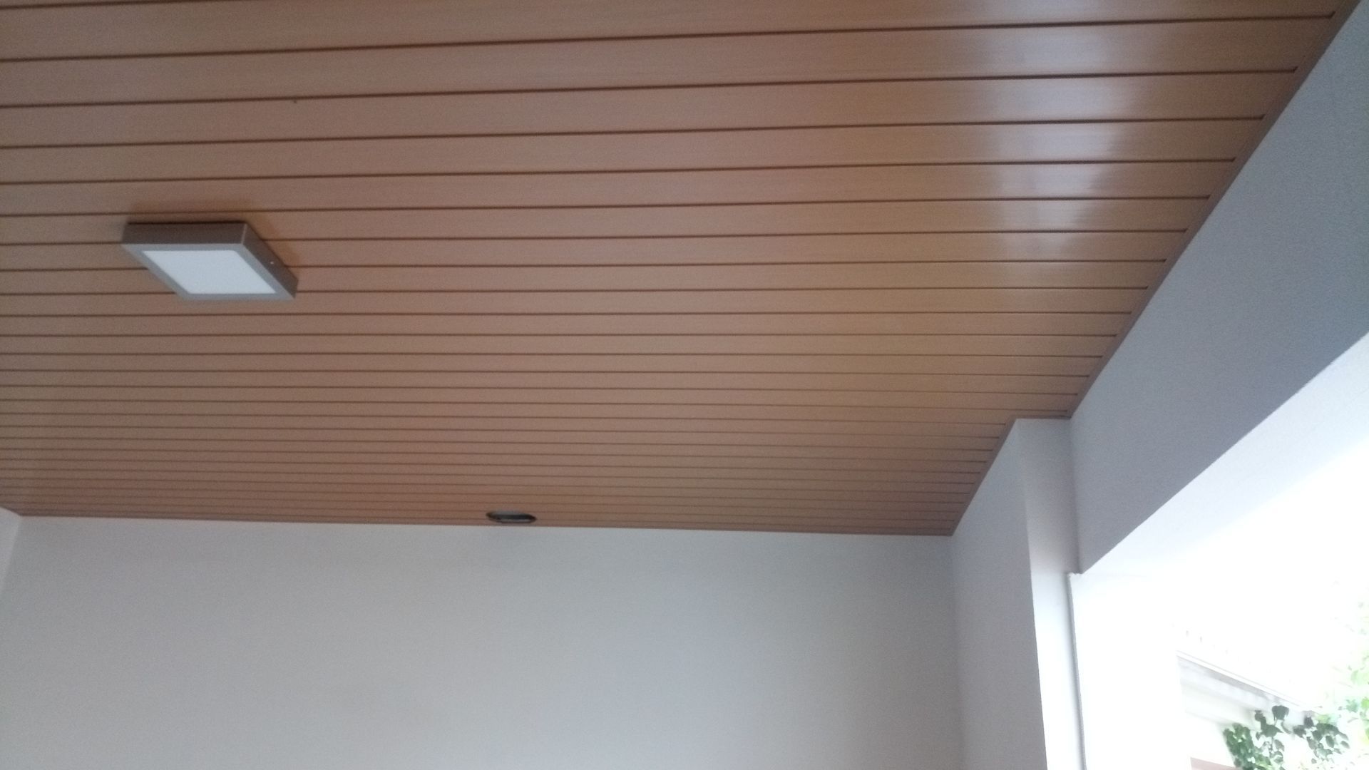 Teto com painéis de madeira, luminária quadrada e paredes brancas.