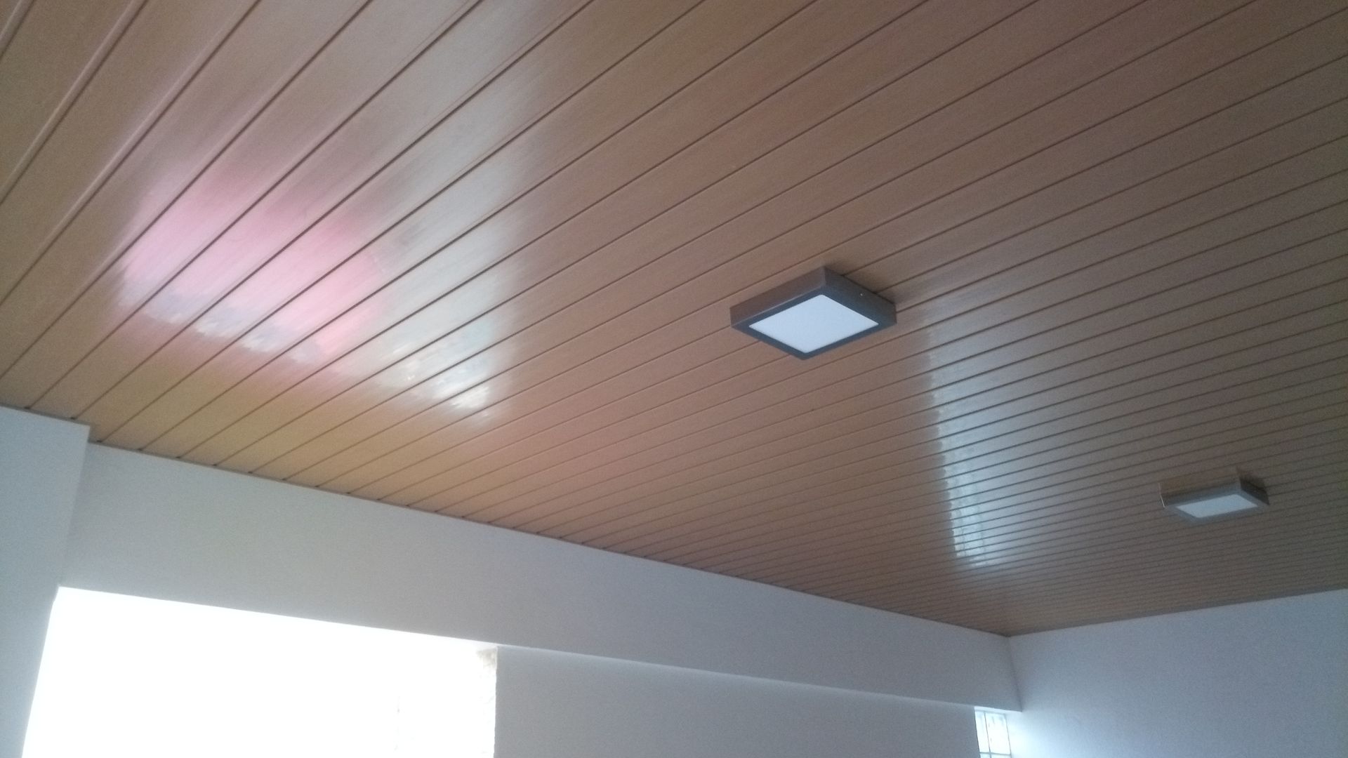 Teto com painéis marrons e duas luminárias quadradas de teto com iluminação branca.