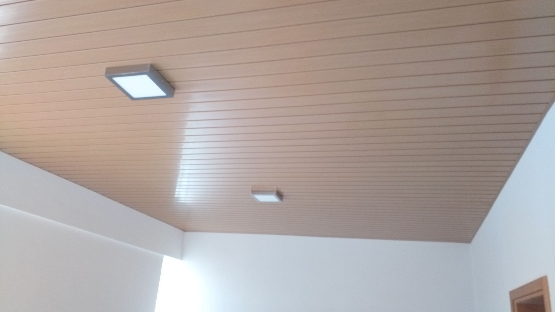 Teto com painéis imitando madeira e duas luminárias quadradas; paredes brancas nos cantos.