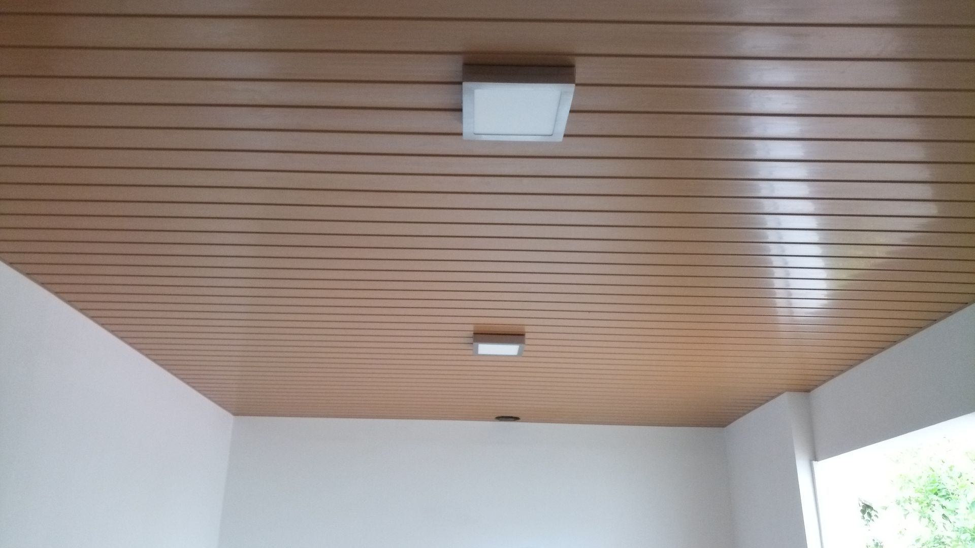 Teto com ripas de madeira e duas luminárias quadradas brancas. Paredes brancas.